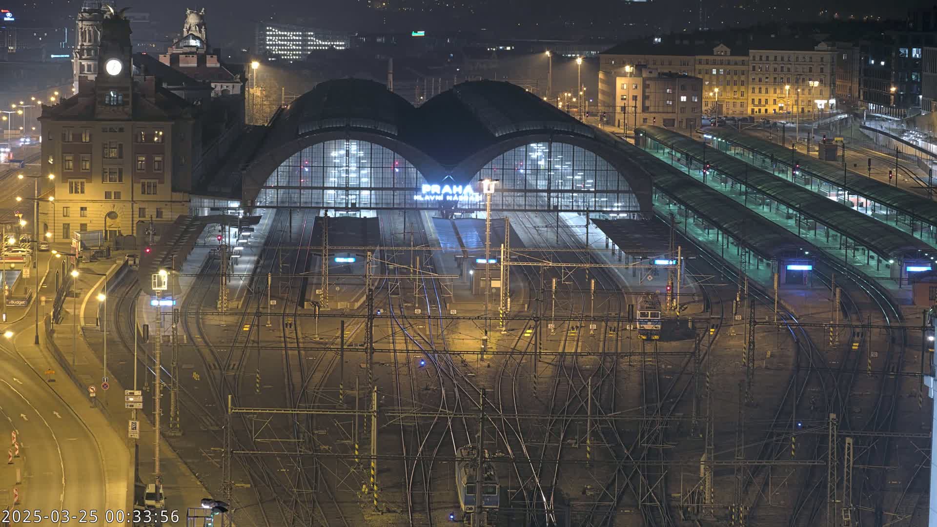 A large, illuminated train station at night, surrounded by numerous tracks and platforms.