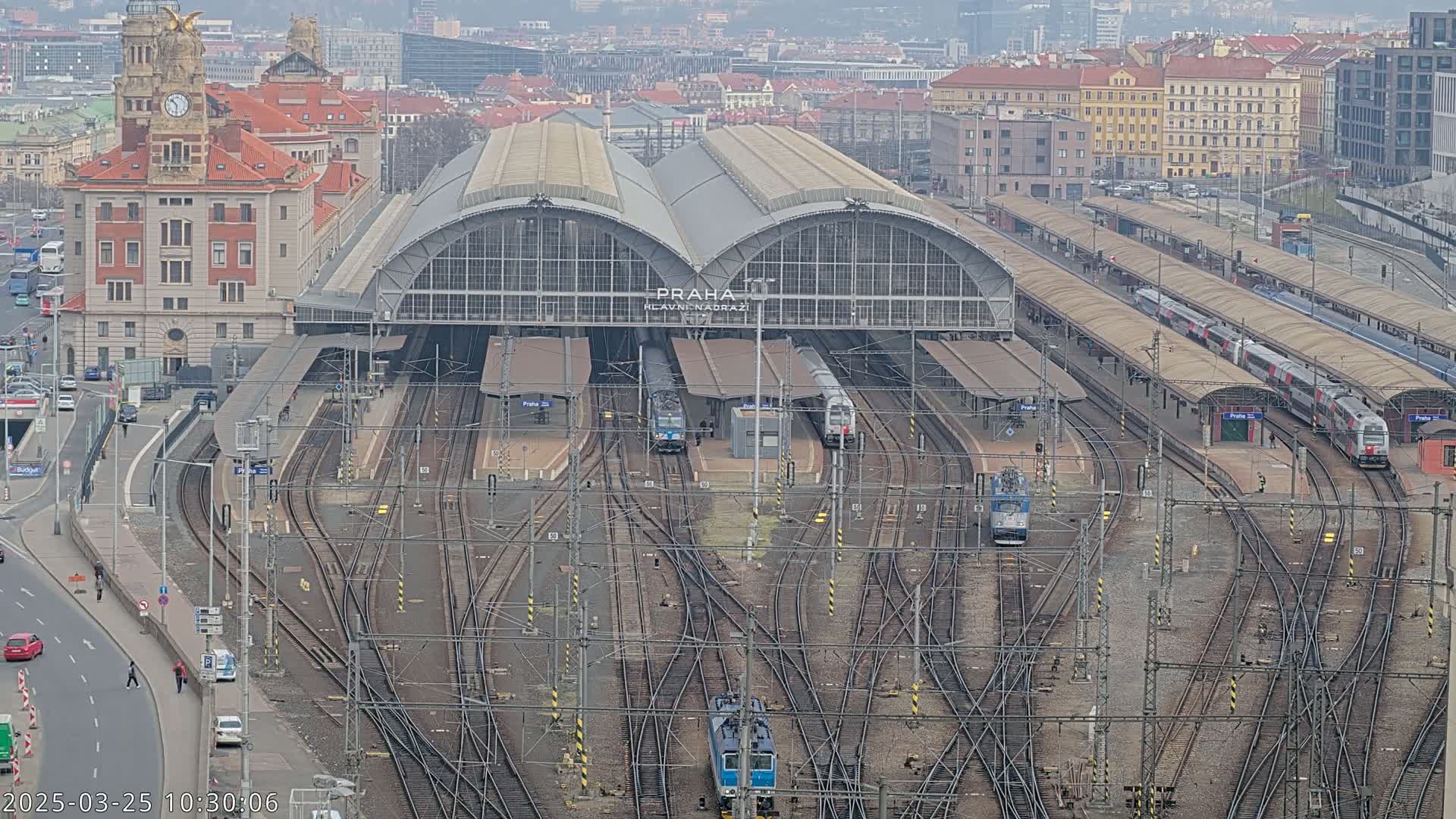 A large train station with multiple trains and tracks, situated in a city on an overcast day.