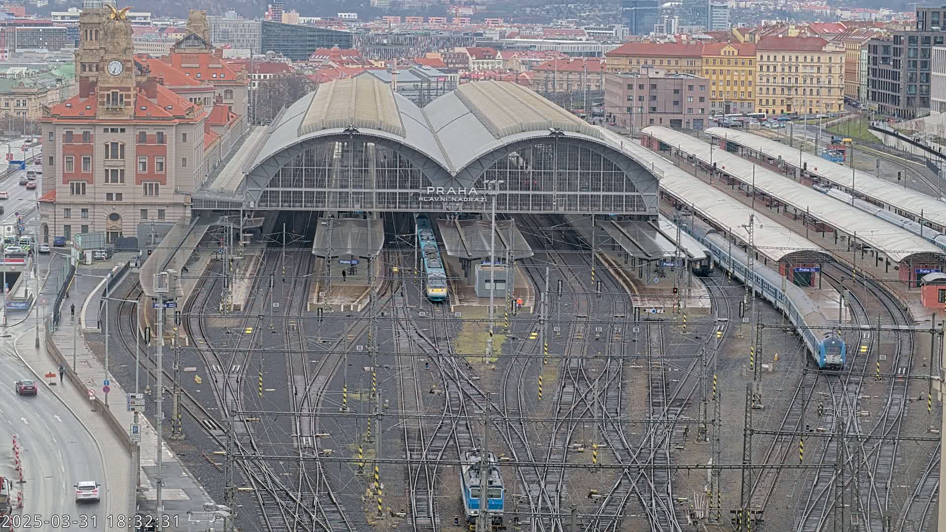 A large train station with numerous tracks and several trains, situated in a city on an overcast day.