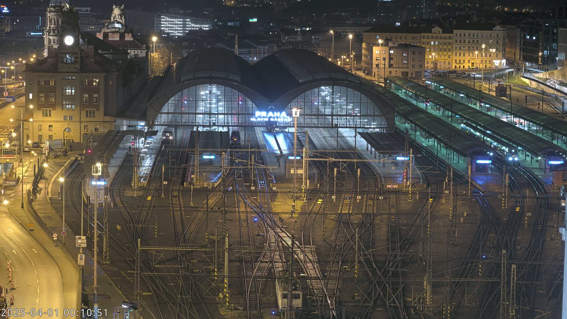 A large, illuminated train station at night, surrounded by a complex network of train tracks.