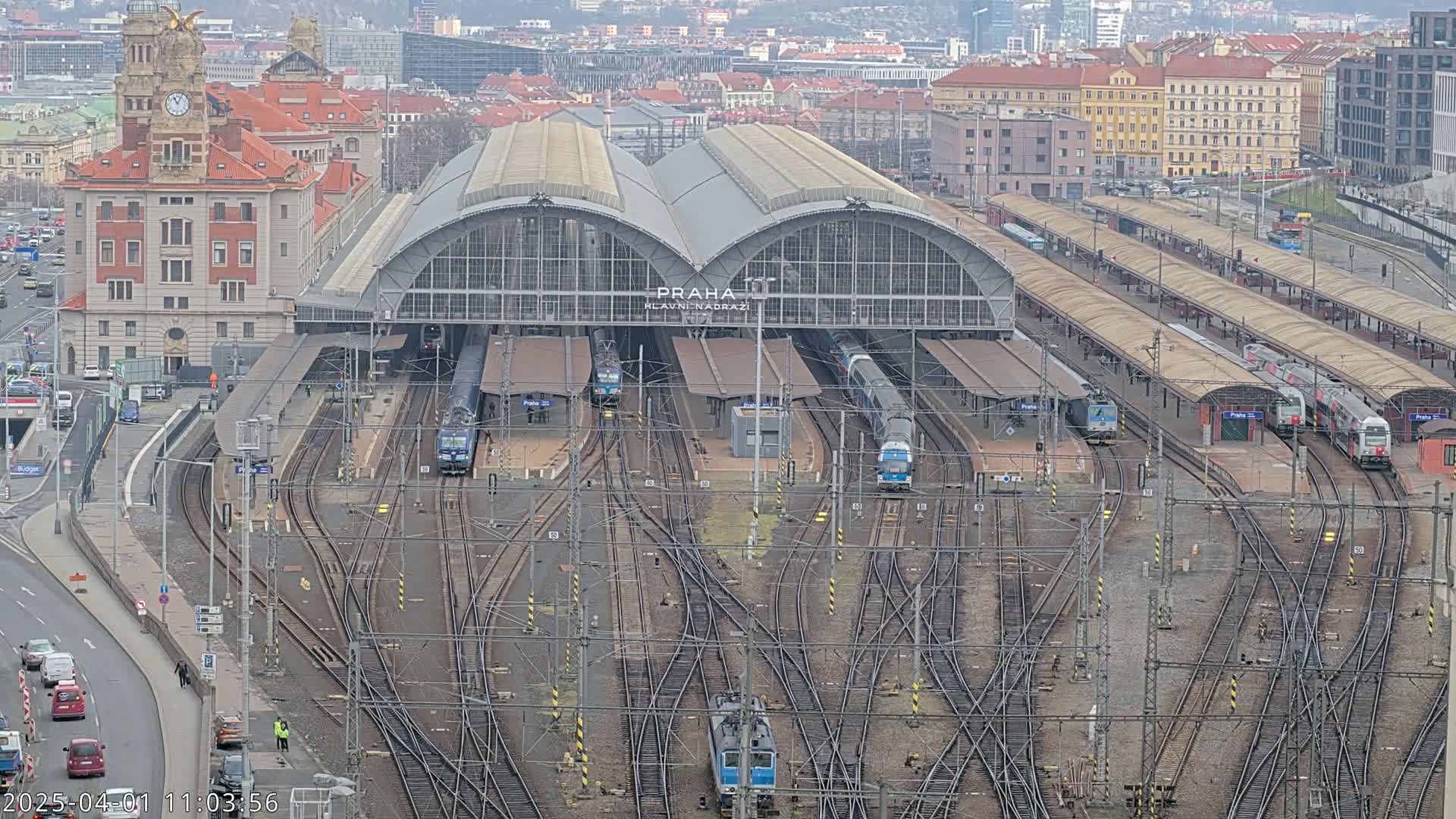 A large train station with numerous tracks and trains, under an overcast sky.