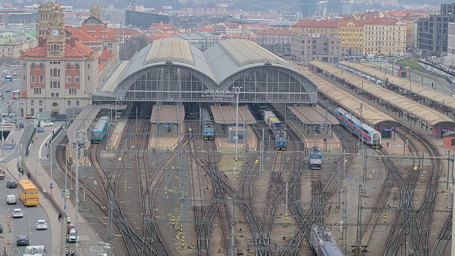 A large train station with numerous tracks and trains, viewed from above on an overcast day.
