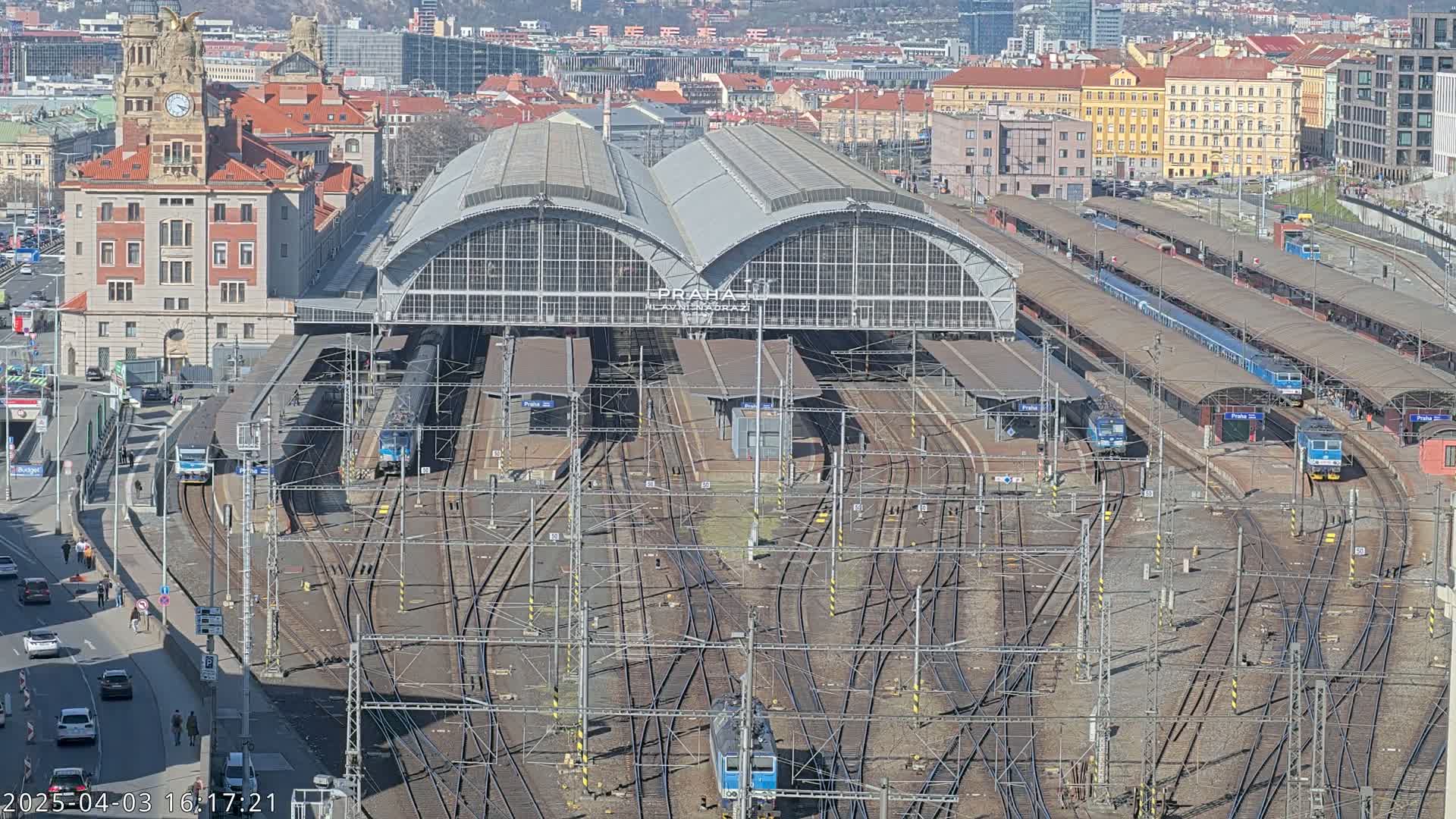 A large train station with numerous tracks and several trains, under a sunny sky.