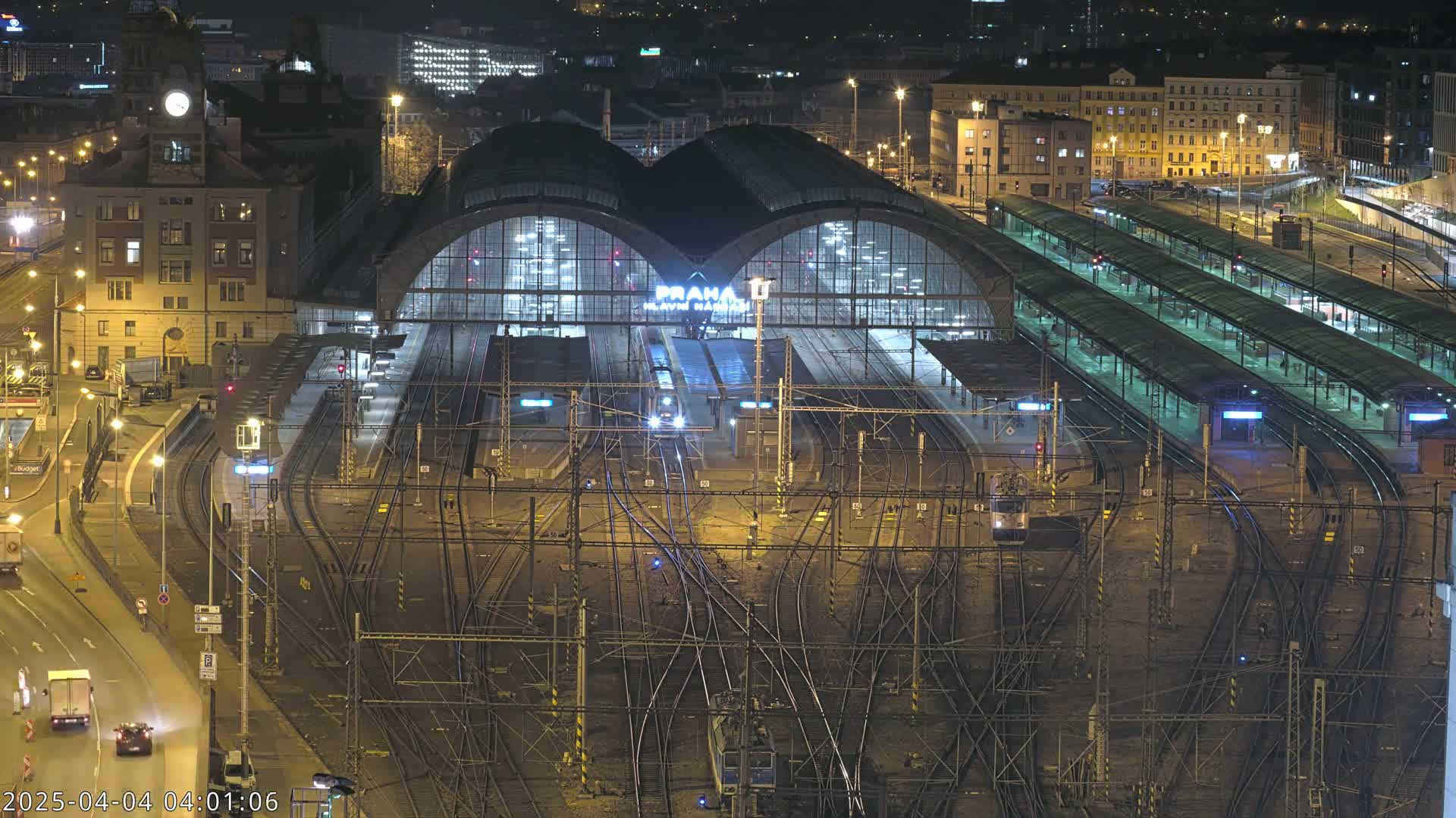 A brightly lit train station at night, with numerous train tracks and platforms extending from a large central building.