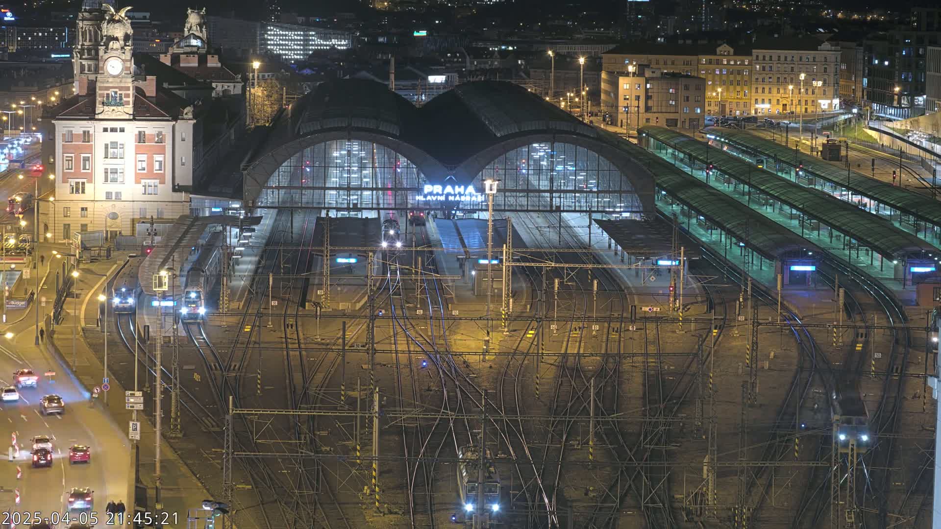 A nighttime aerial view of a busy train station with numerous tracks and trains, illuminated by streetlights and the station's lights.