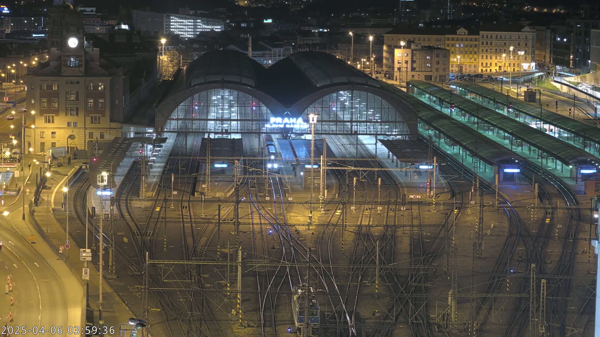 A nighttime, high-angle view of a large, illuminated train station with numerous tracks and platforms.
