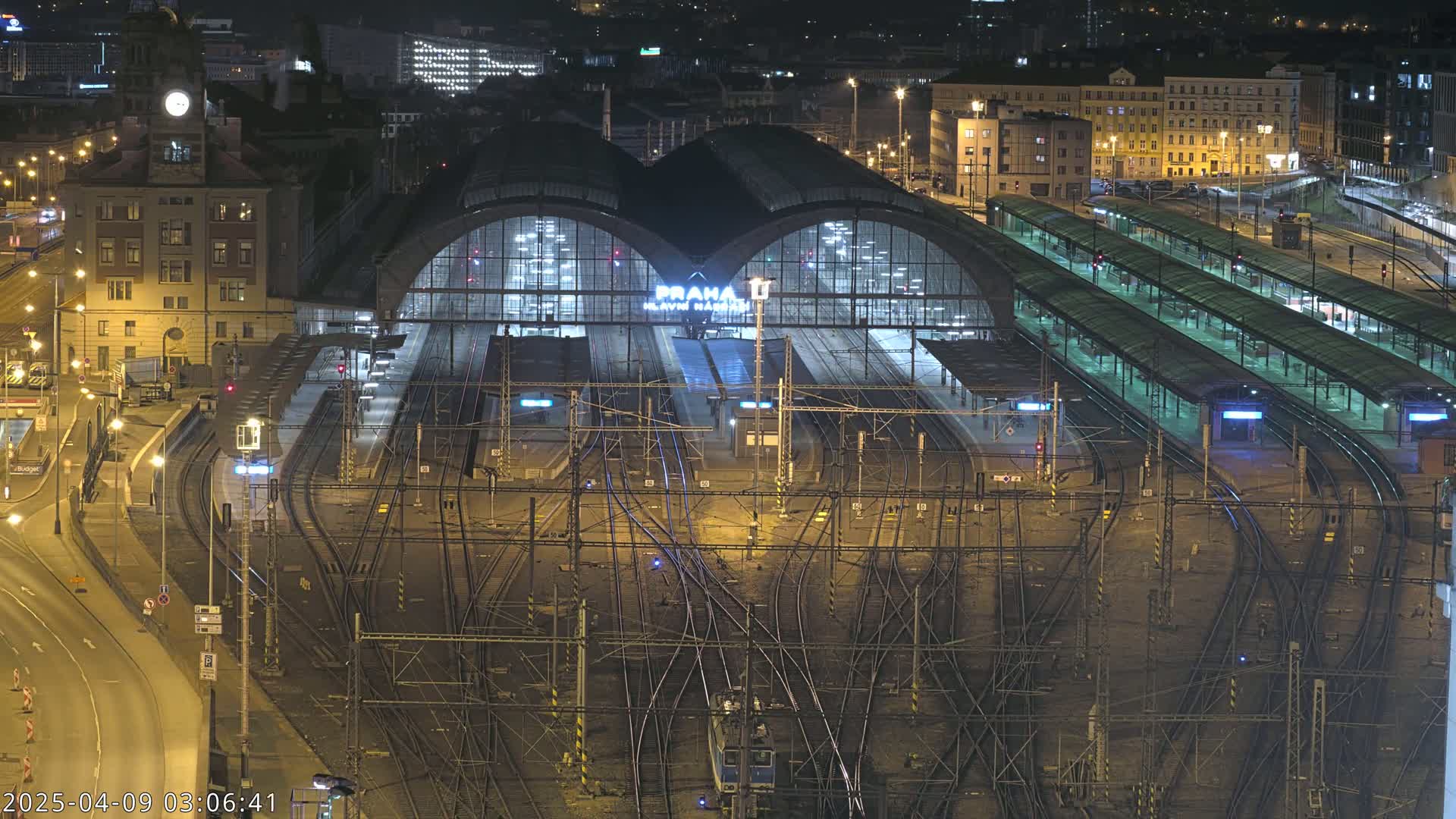 A large, illuminated train station at night, surrounded by a complex network of train tracks and city buildings.