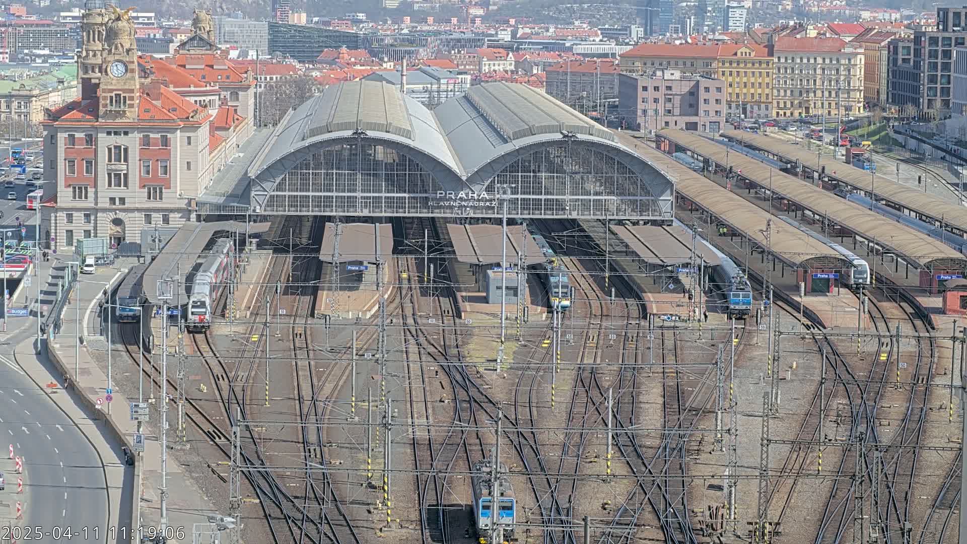A large train station with numerous tracks and trains under a sunny sky.