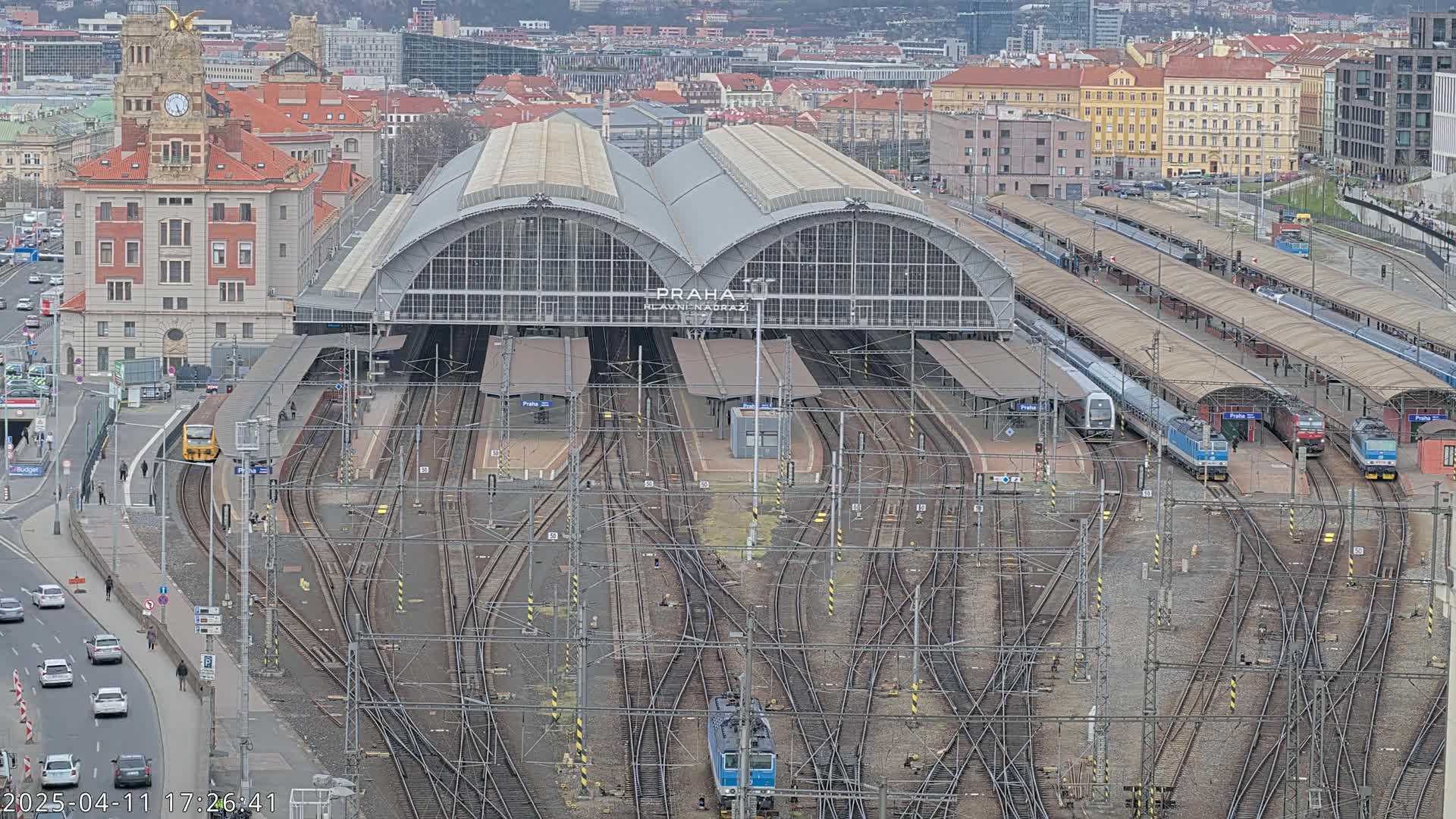 A large train station with numerous tracks and trains, situated in a city under an overcast sky.