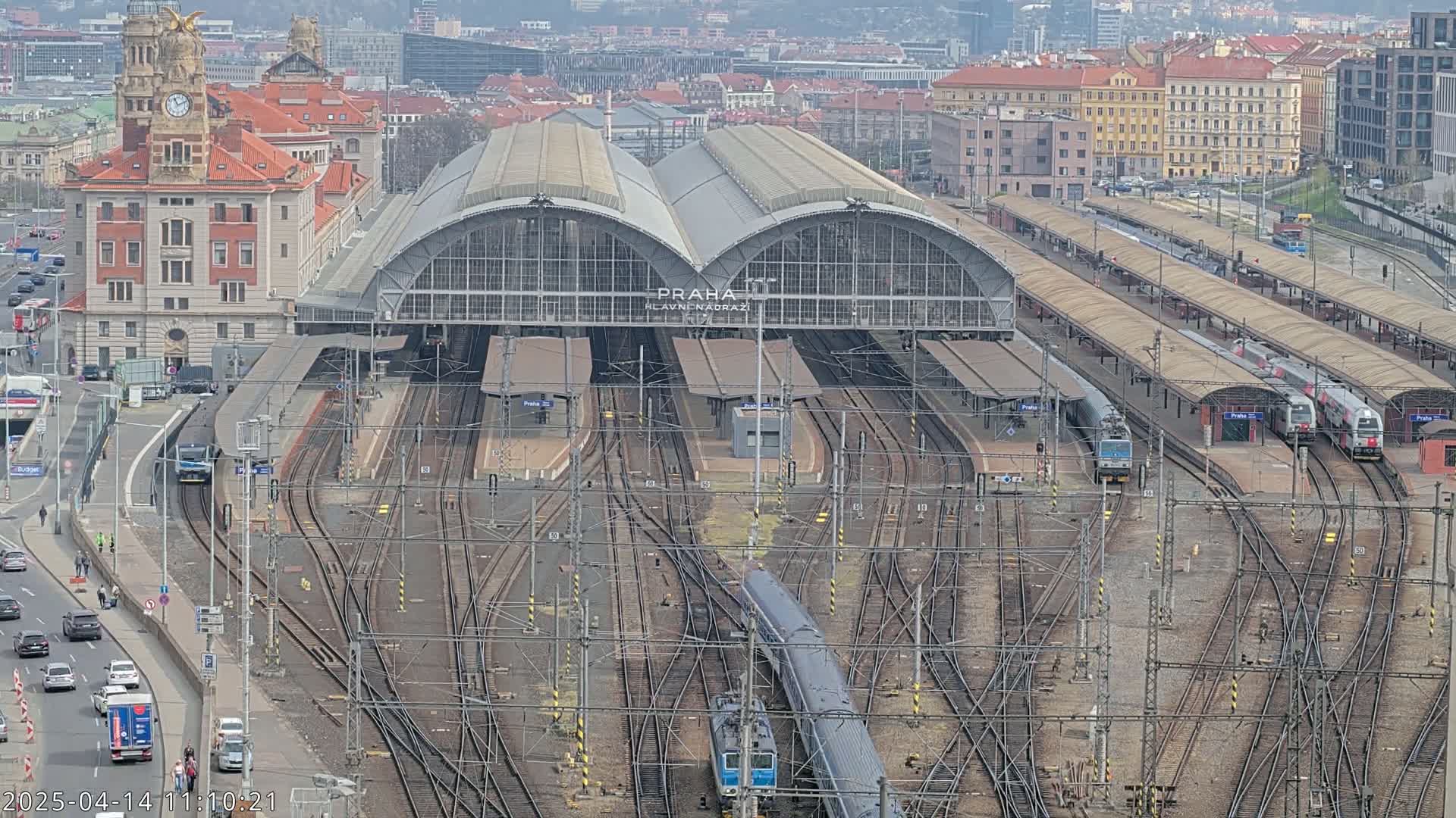 A large train station with numerous tracks and trains, under a mostly cloudy sky.