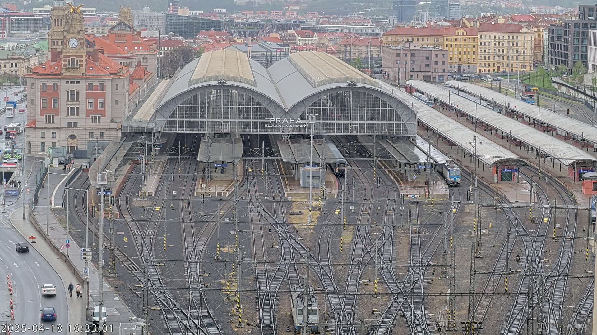 A large train station with numerous tracks and platforms, surrounded by city buildings under an overcast sky.