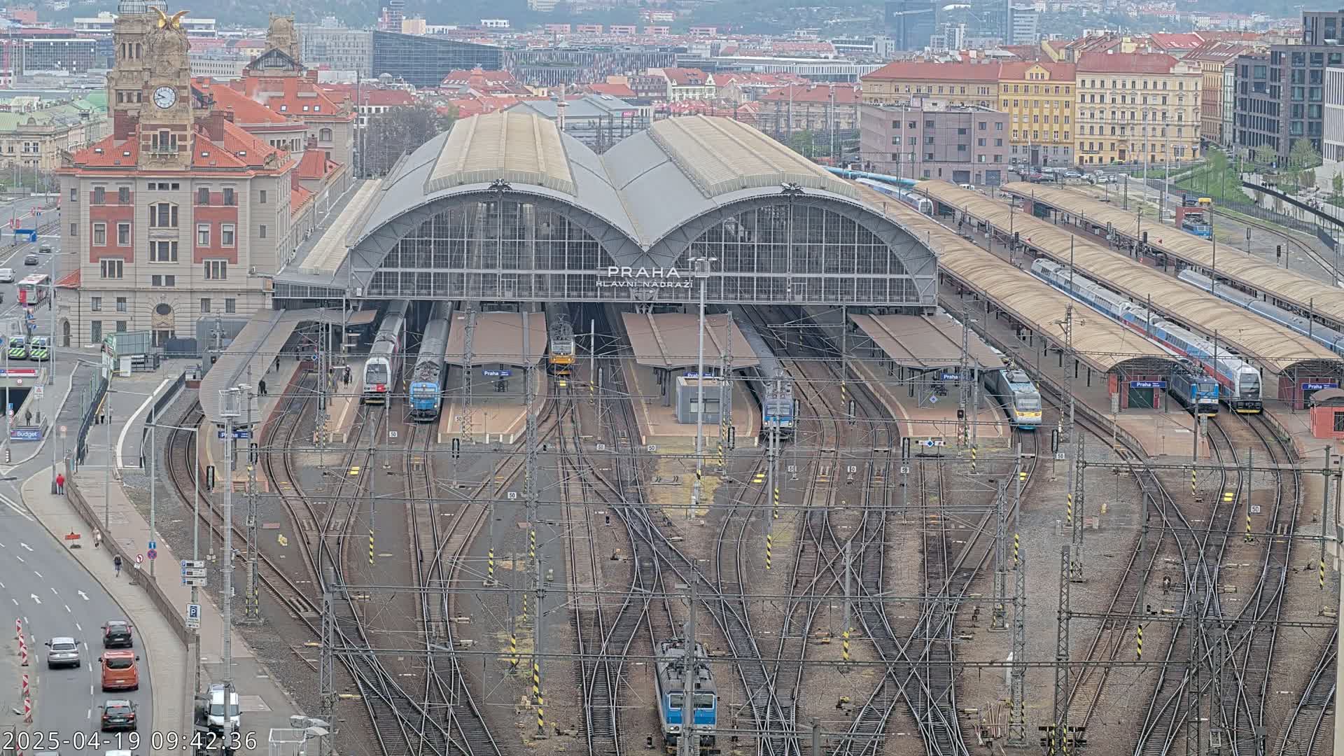 A large train station with many tracks and several trains, situated in a city on an overcast day.