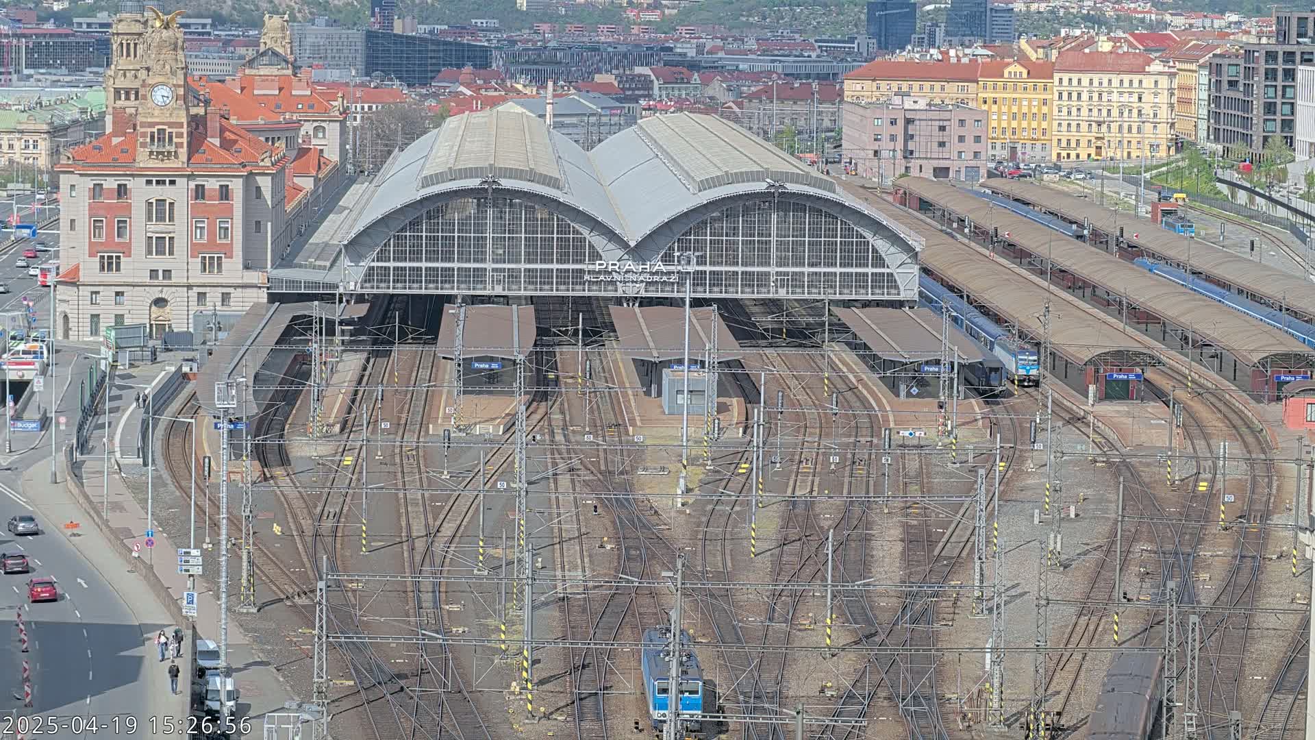 A large train station with many tracks and platforms, surrounded by city buildings on a sunny day.