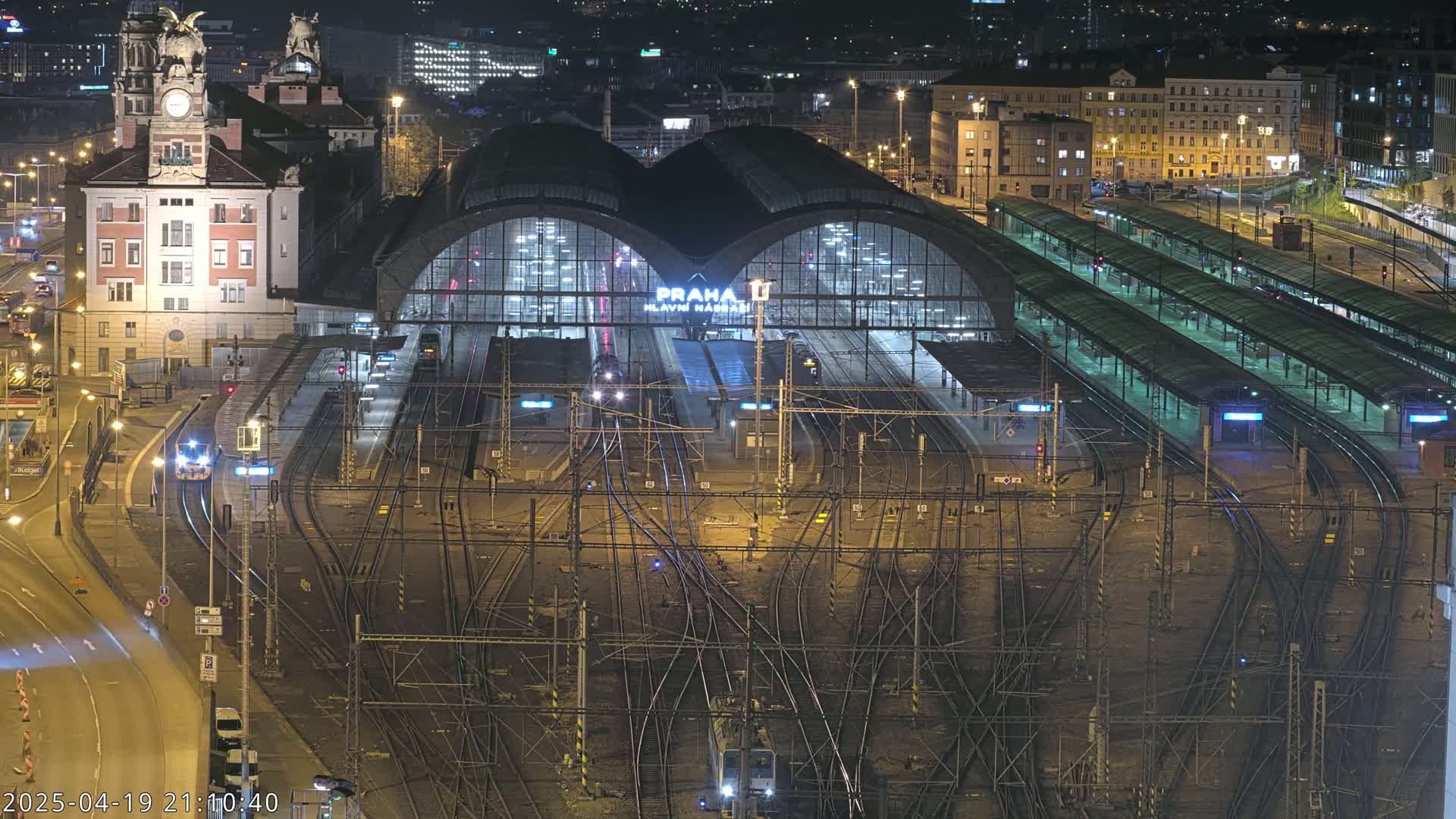 A large, illuminated train station at night, with numerous train tracks and platforms extending from it.
