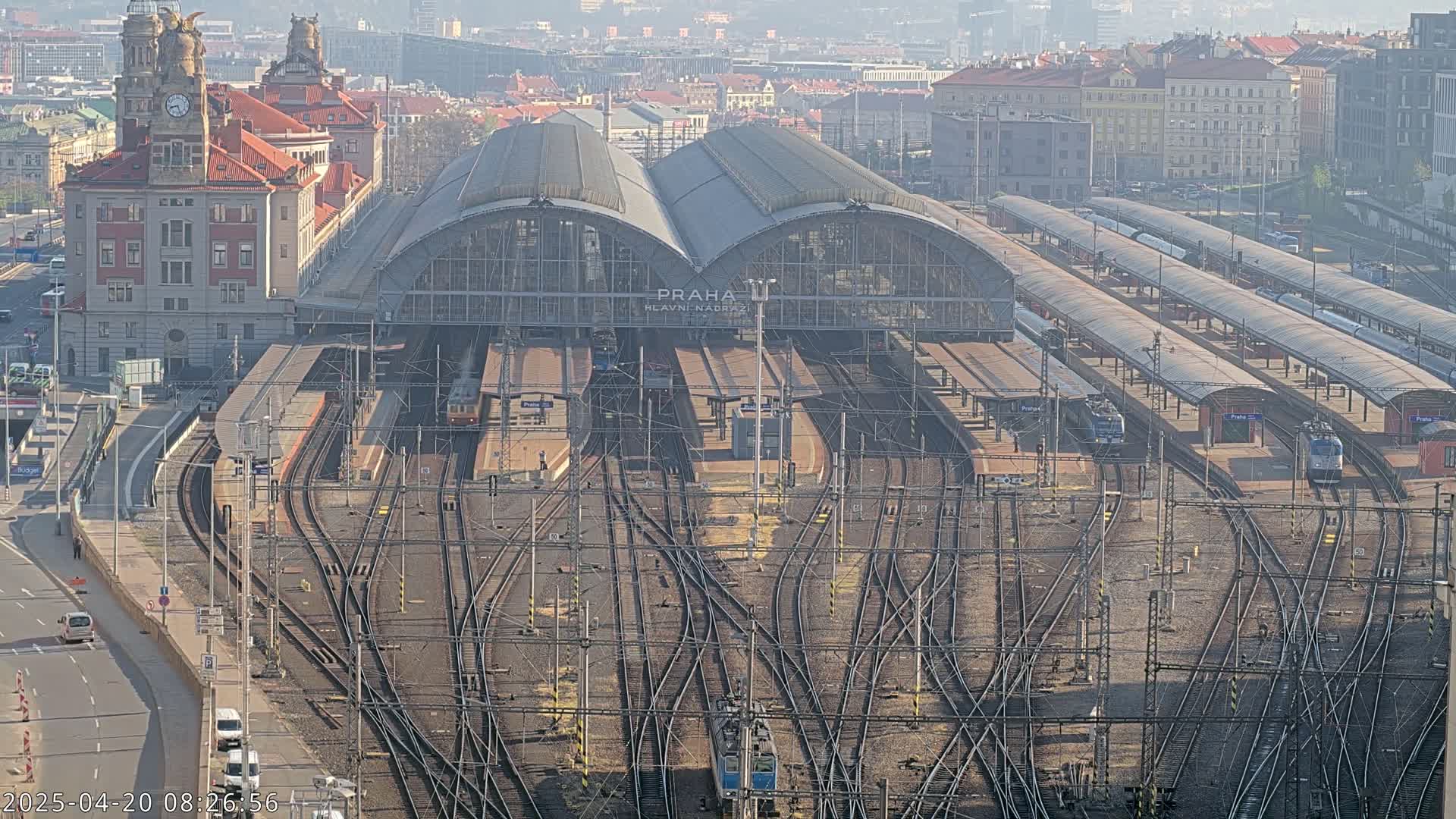 A large train station with numerous tracks and trains, situated in a city on a hazy day.