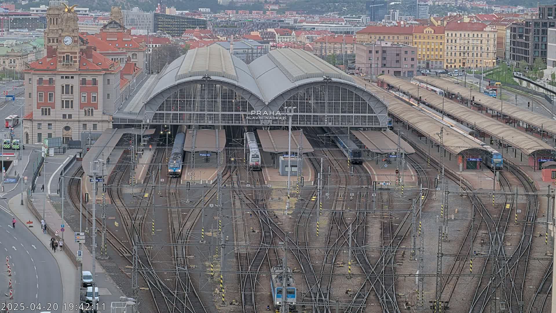 A large train station with multiple trains at various platforms, surrounded by a city under an overcast sky.