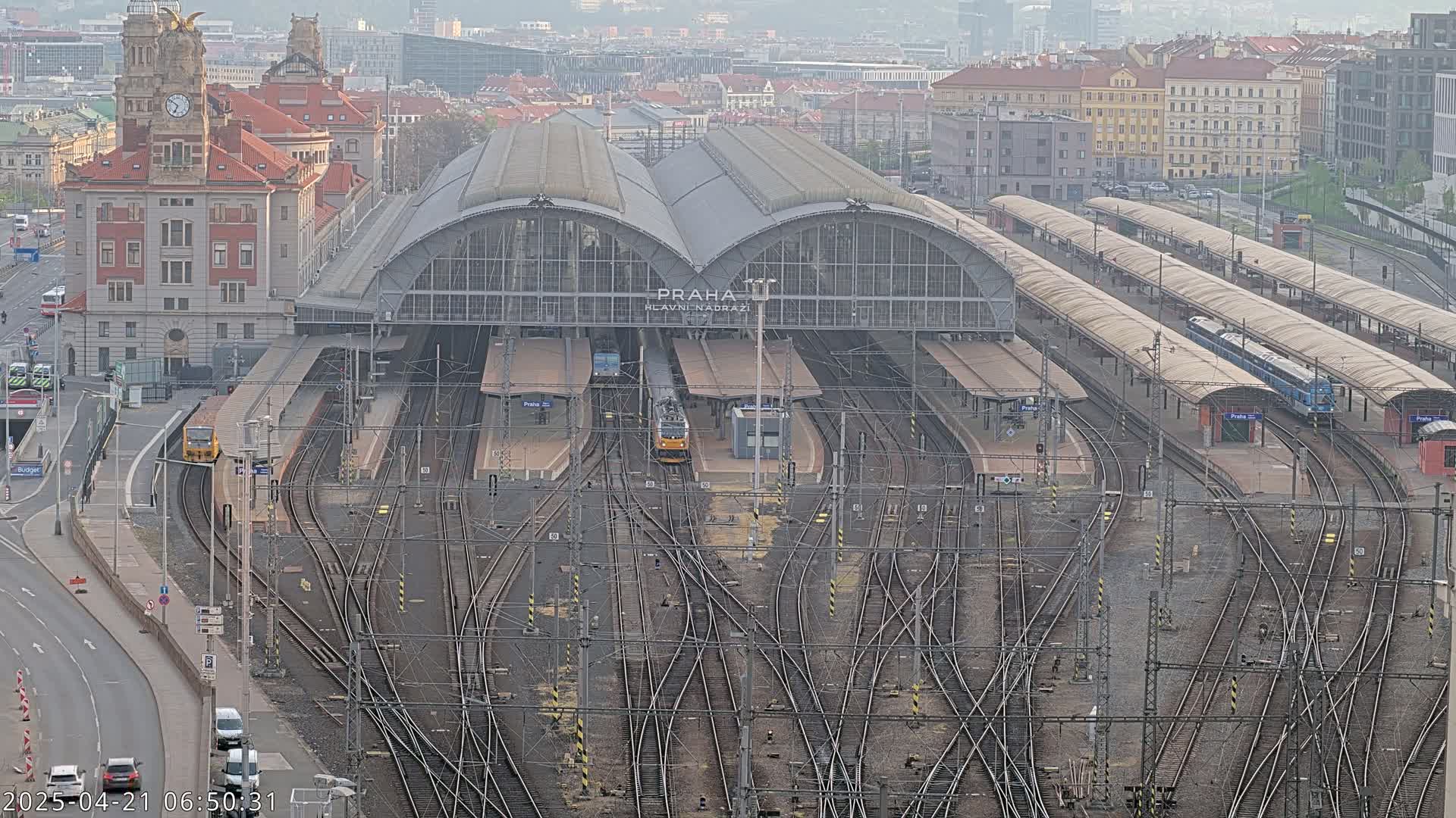 A large train station with numerous tracks and trains, situated in a city under an overcast sky.