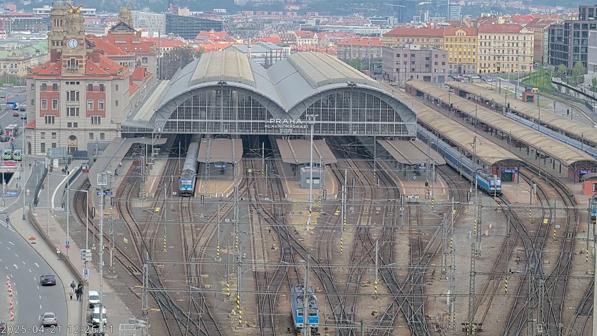 An aerial view shows a large train station with numerous tracks and trains, under an overcast sky.