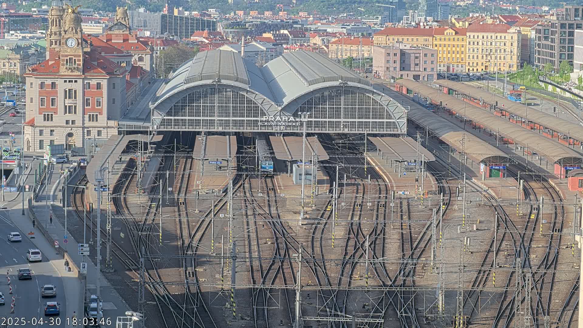 An aerial view of a large train station with many tracks and platforms, under a partly sunny sky.