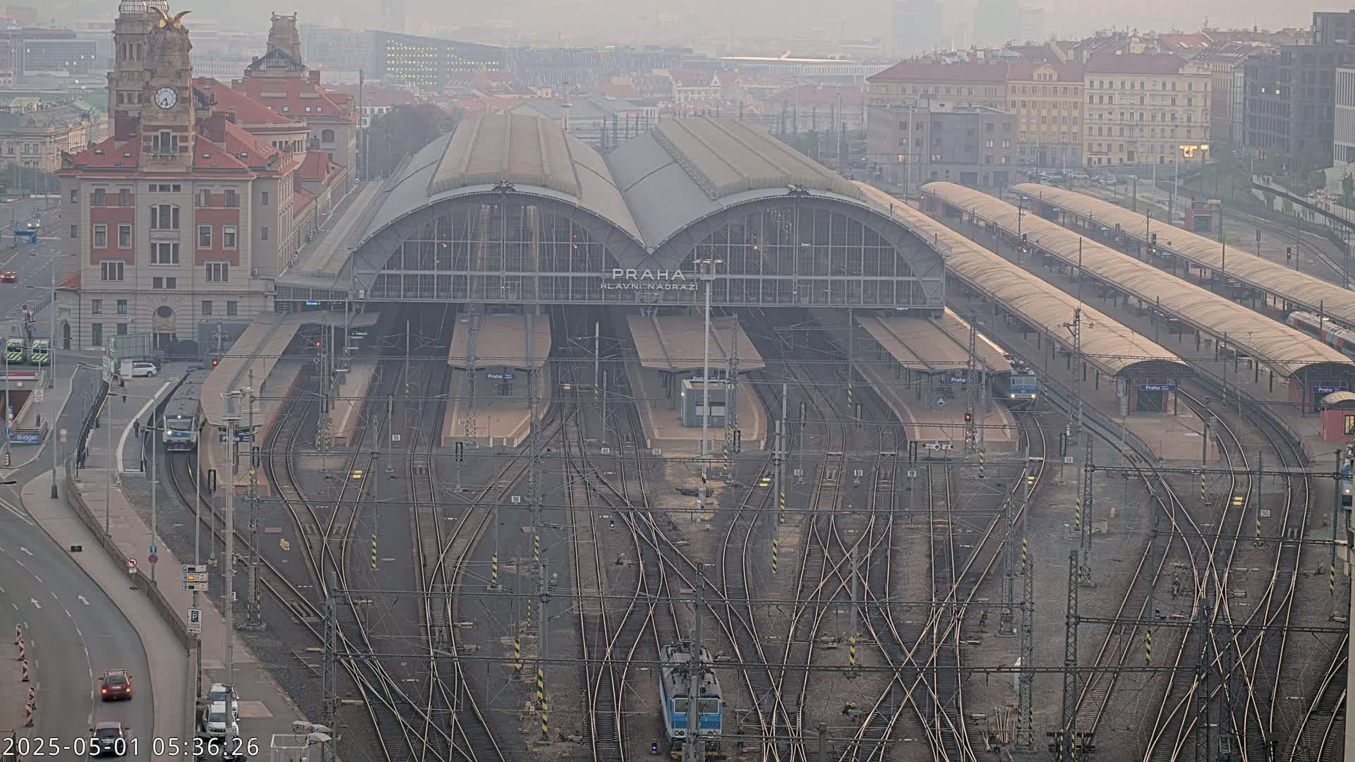 A large train station with numerous tracks and platforms, surrounded by city buildings under hazy conditions.