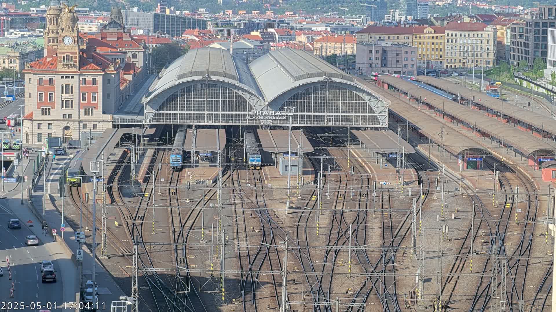 A large train station with numerous tracks and trains, situated in a city on a sunny day.