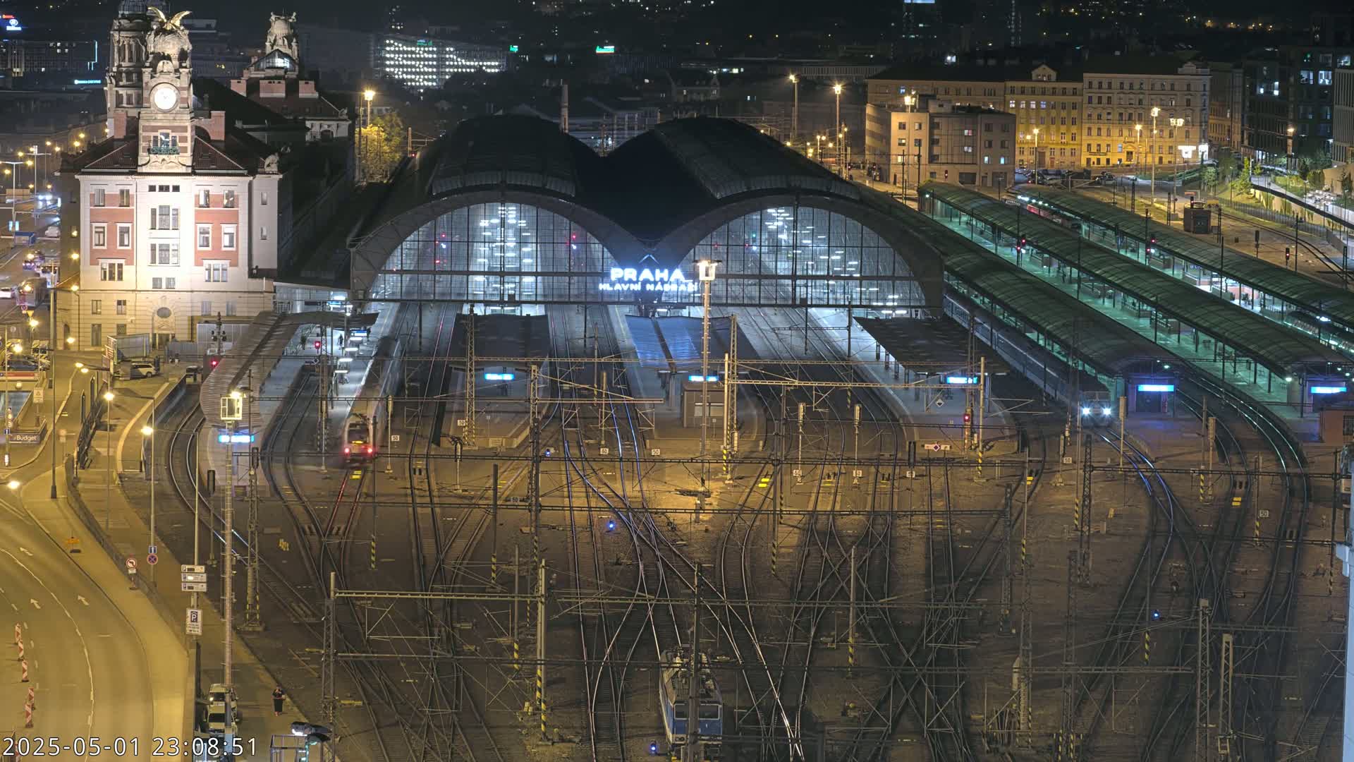 A nighttime aerial view of a bustling train station with numerous tracks and platforms, illuminated by artificial light.