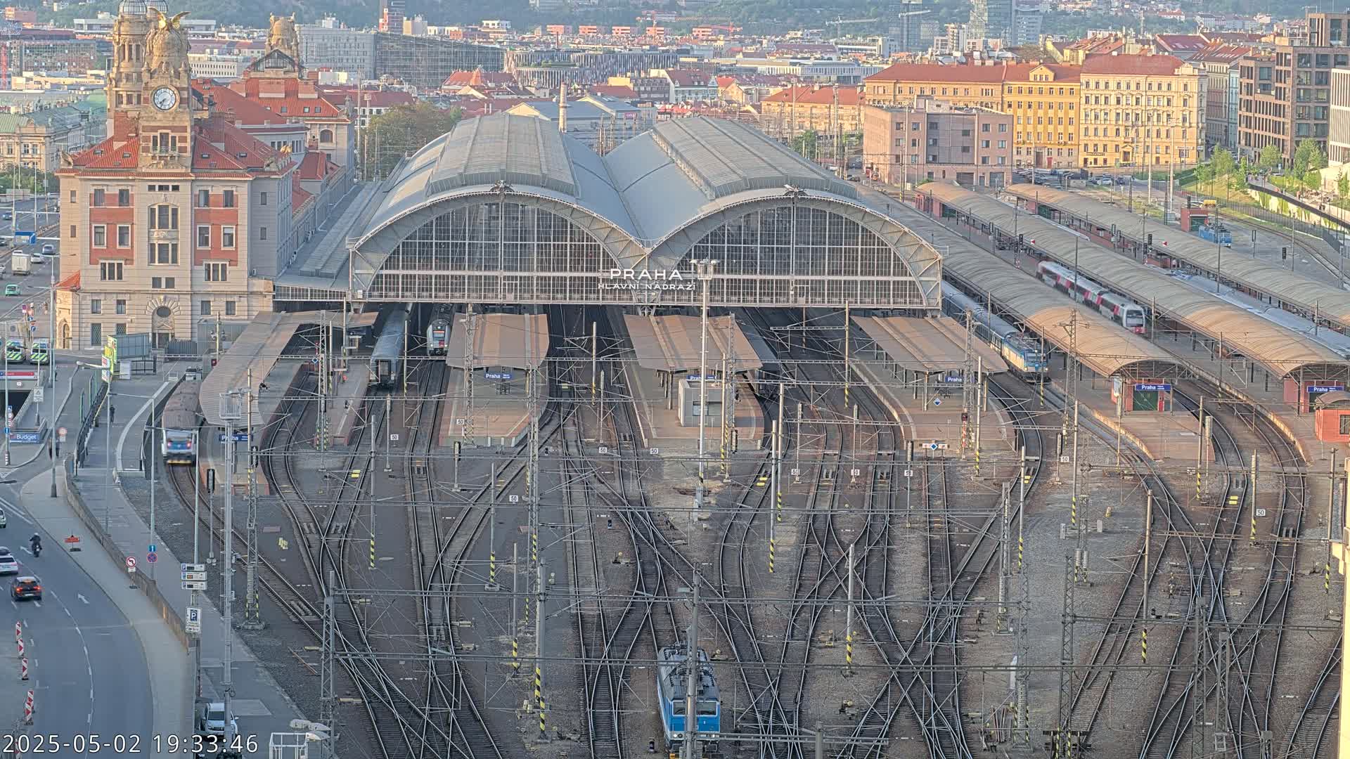 A large train station with numerous tracks and trains, surrounded by a city under a clear sky.
