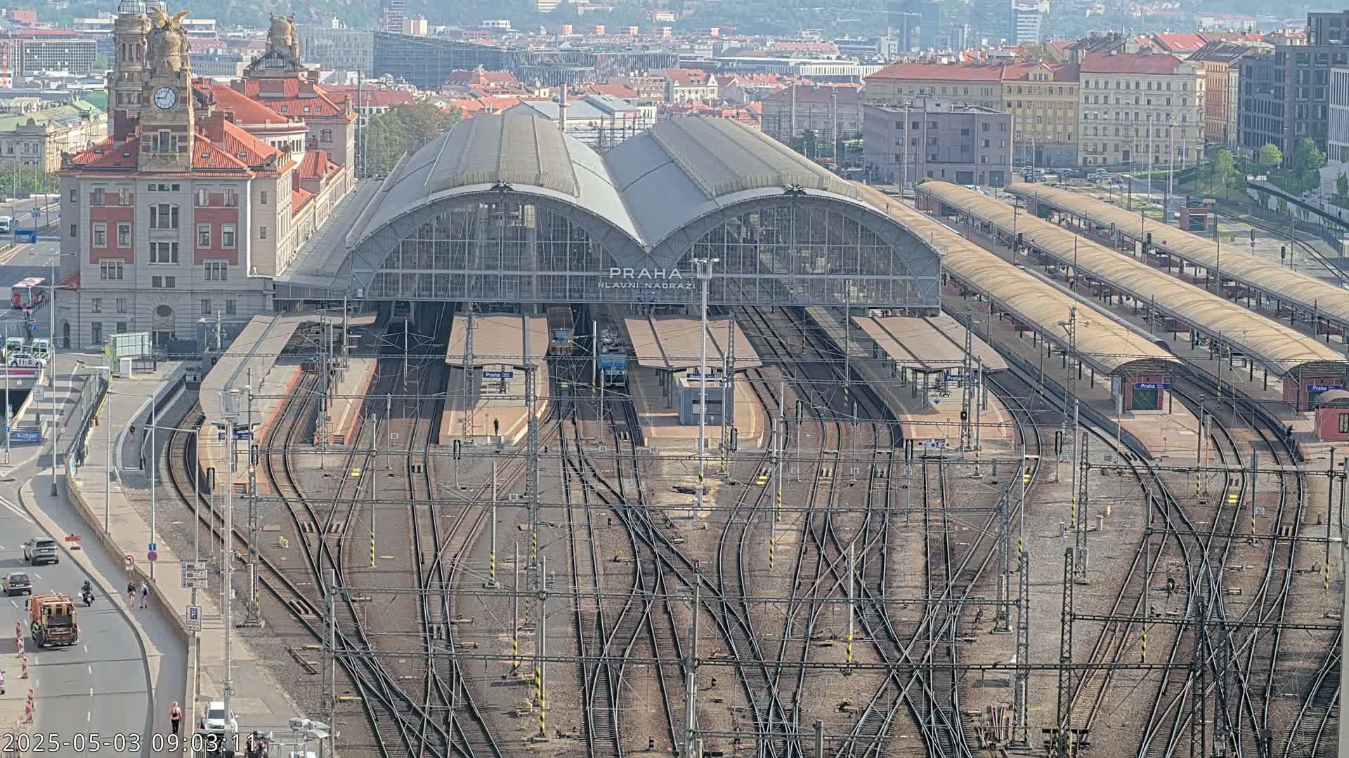 A large train station with numerous tracks and platforms is seen from an aerial view on a sunny day.