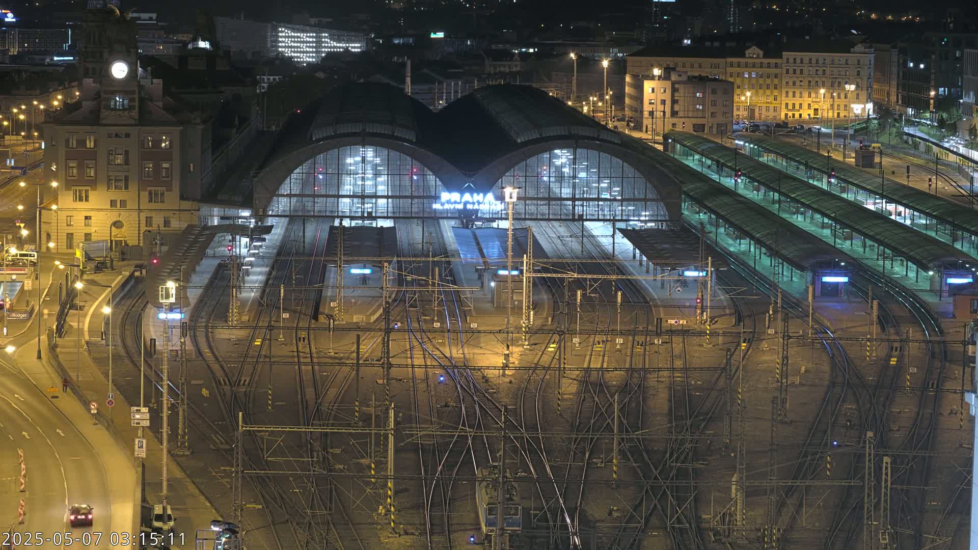 A large, illuminated train station at night with numerous tracks and platforms, surrounded by city buildings.