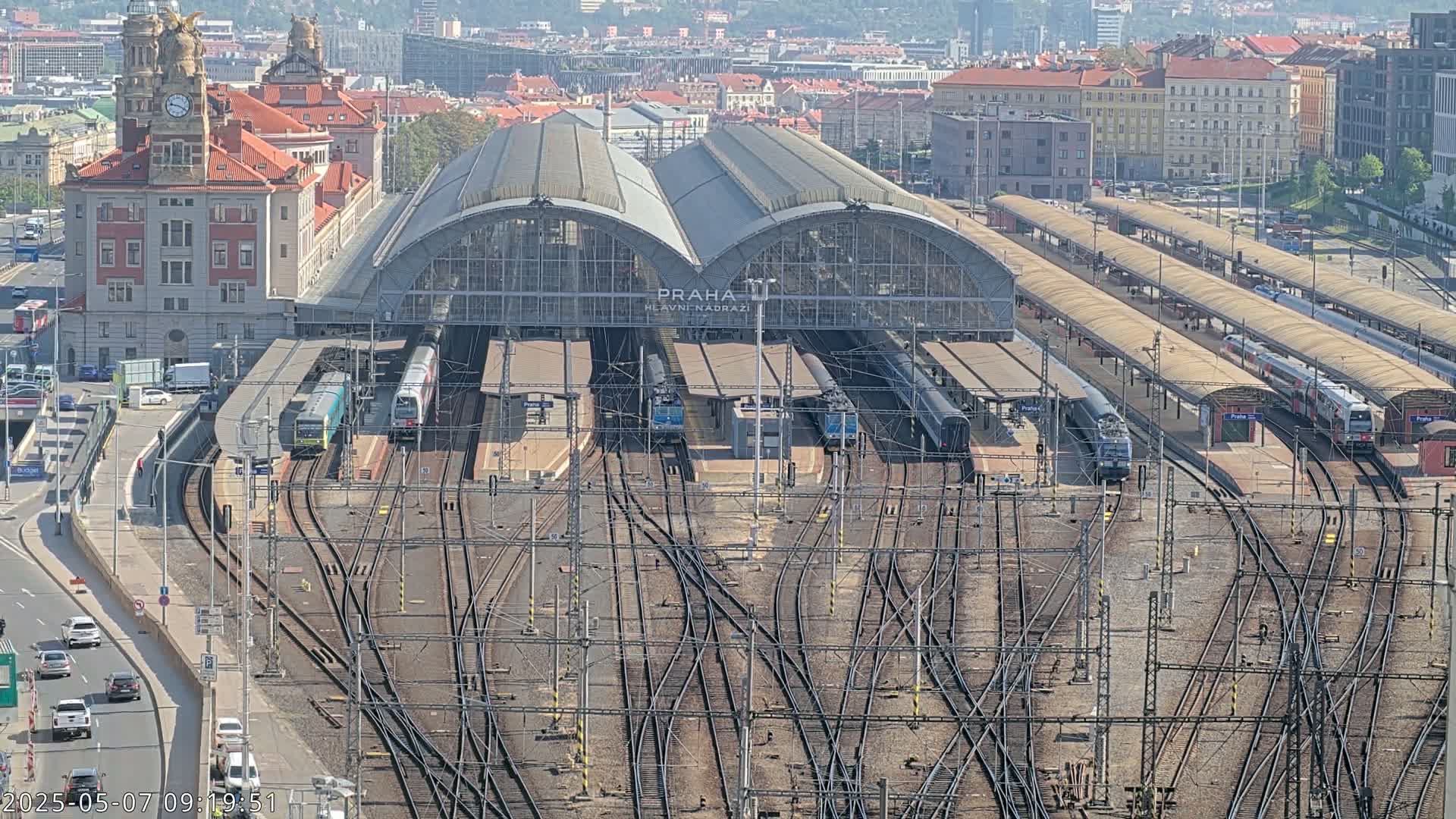 A large train station with many tracks and several trains, under a clear sky.