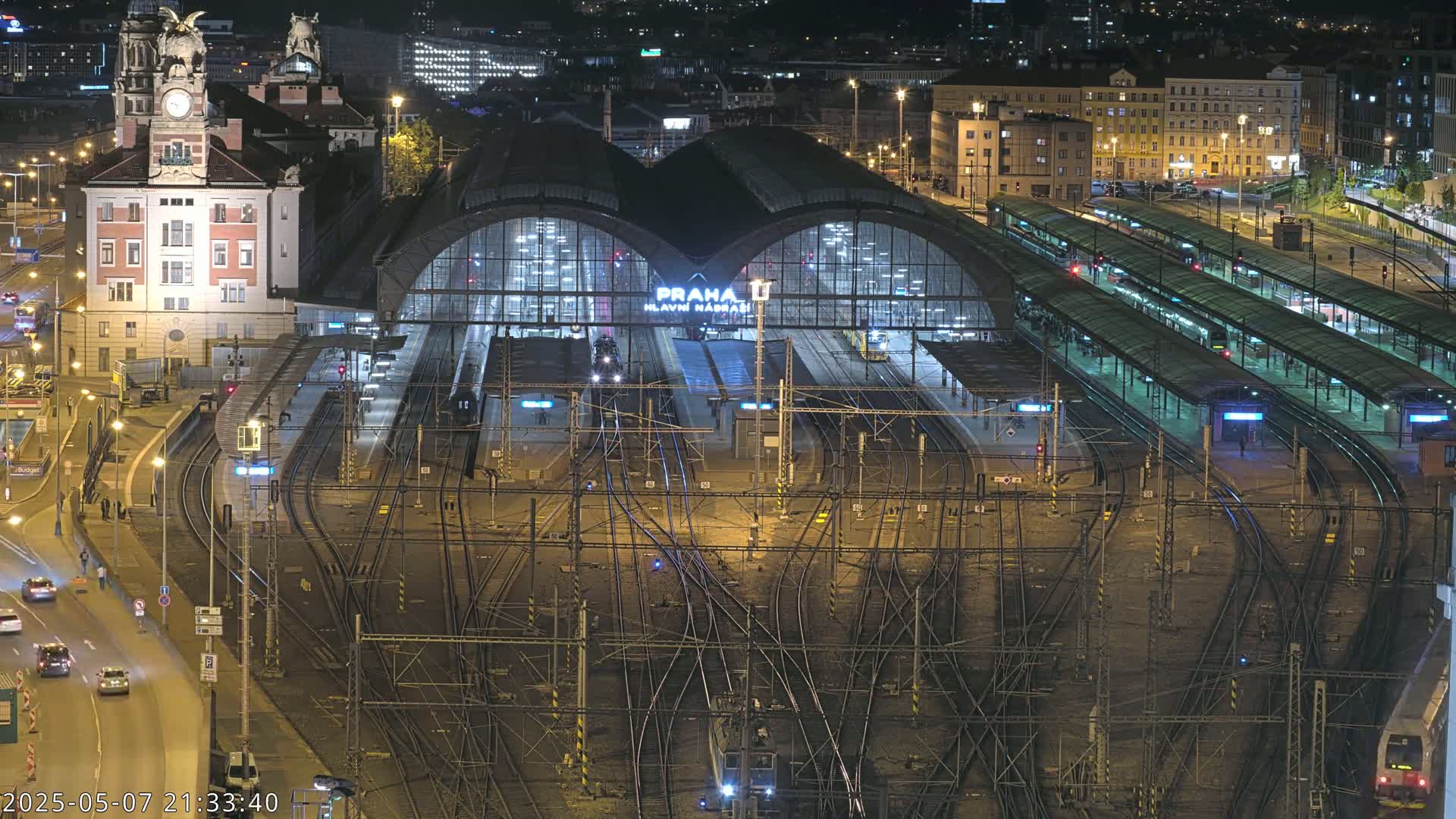 A nighttime aerial view of a busy train station with numerous tracks and platforms illuminated under the city lights.