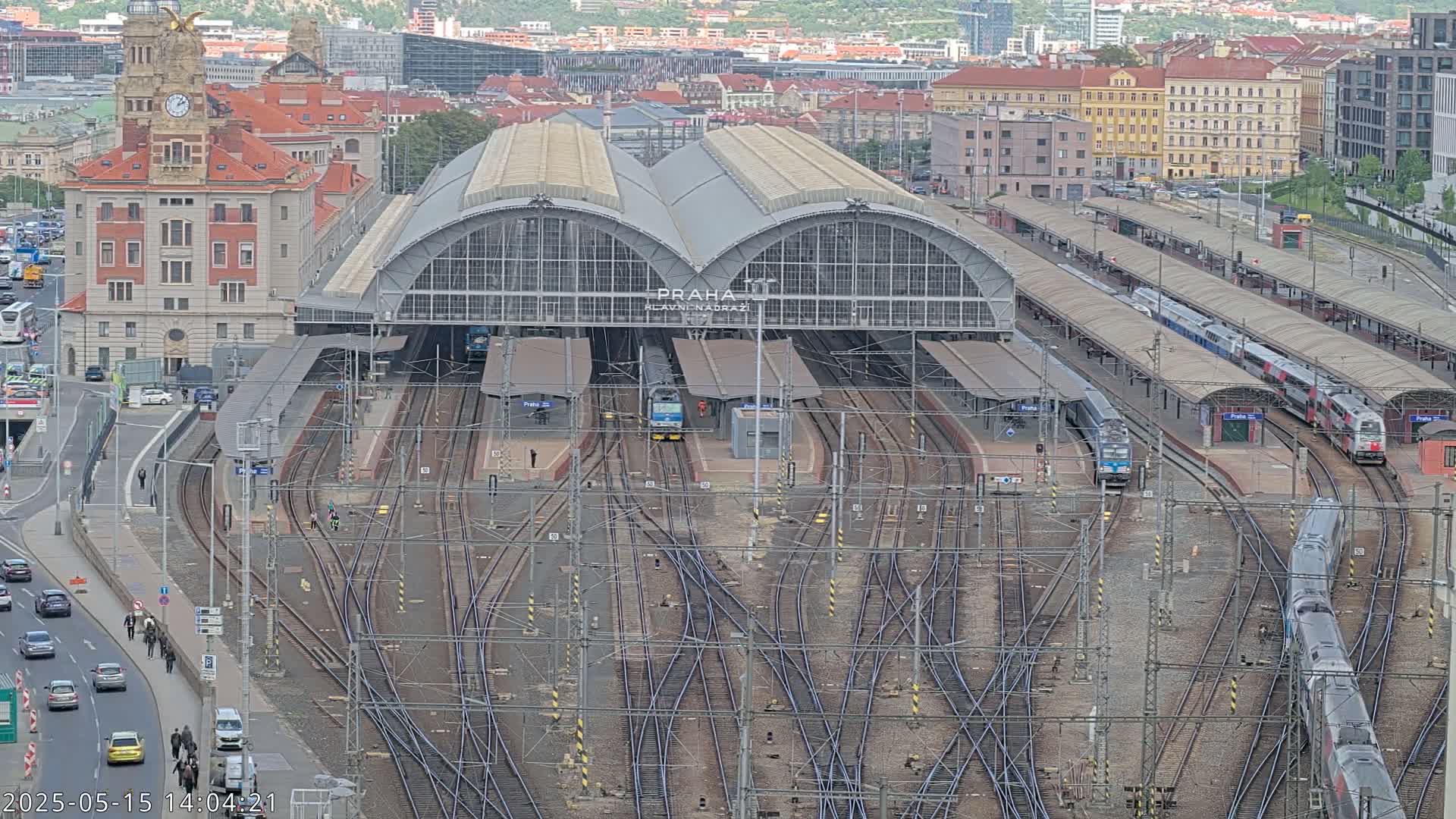 A large train station with numerous tracks and trains, situated in a city under an overcast sky.