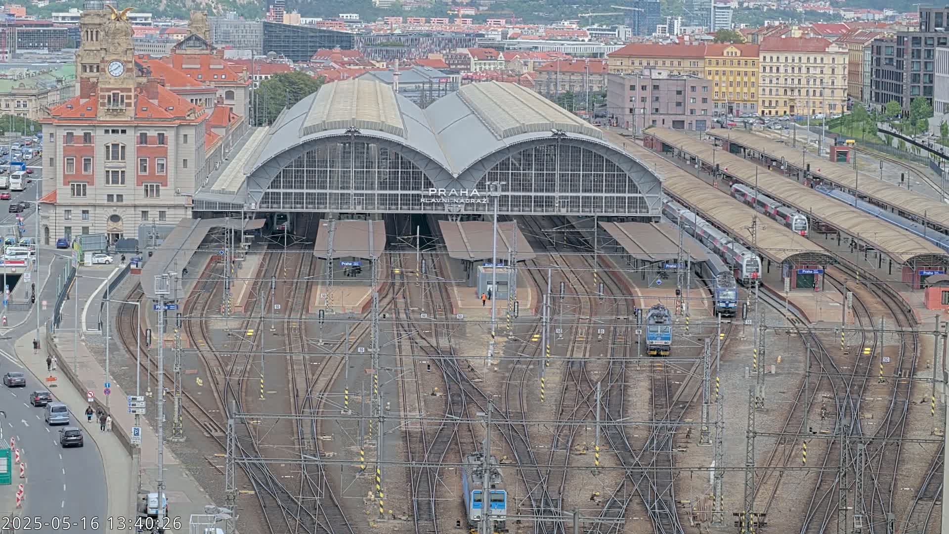 A large train station with numerous tracks and several trains is visible, under an overcast sky.