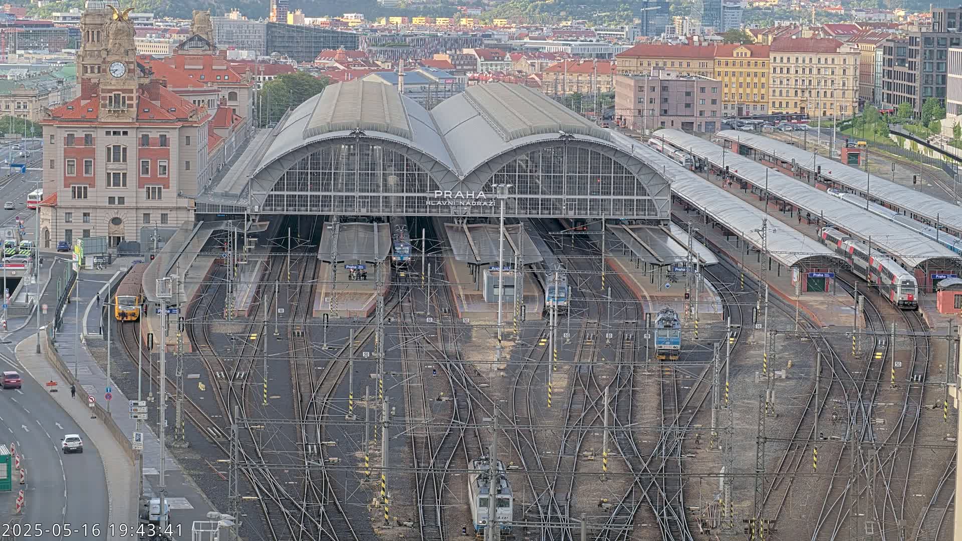 A large train station with many tracks and trains, surrounded by city buildings under an overcast sky.