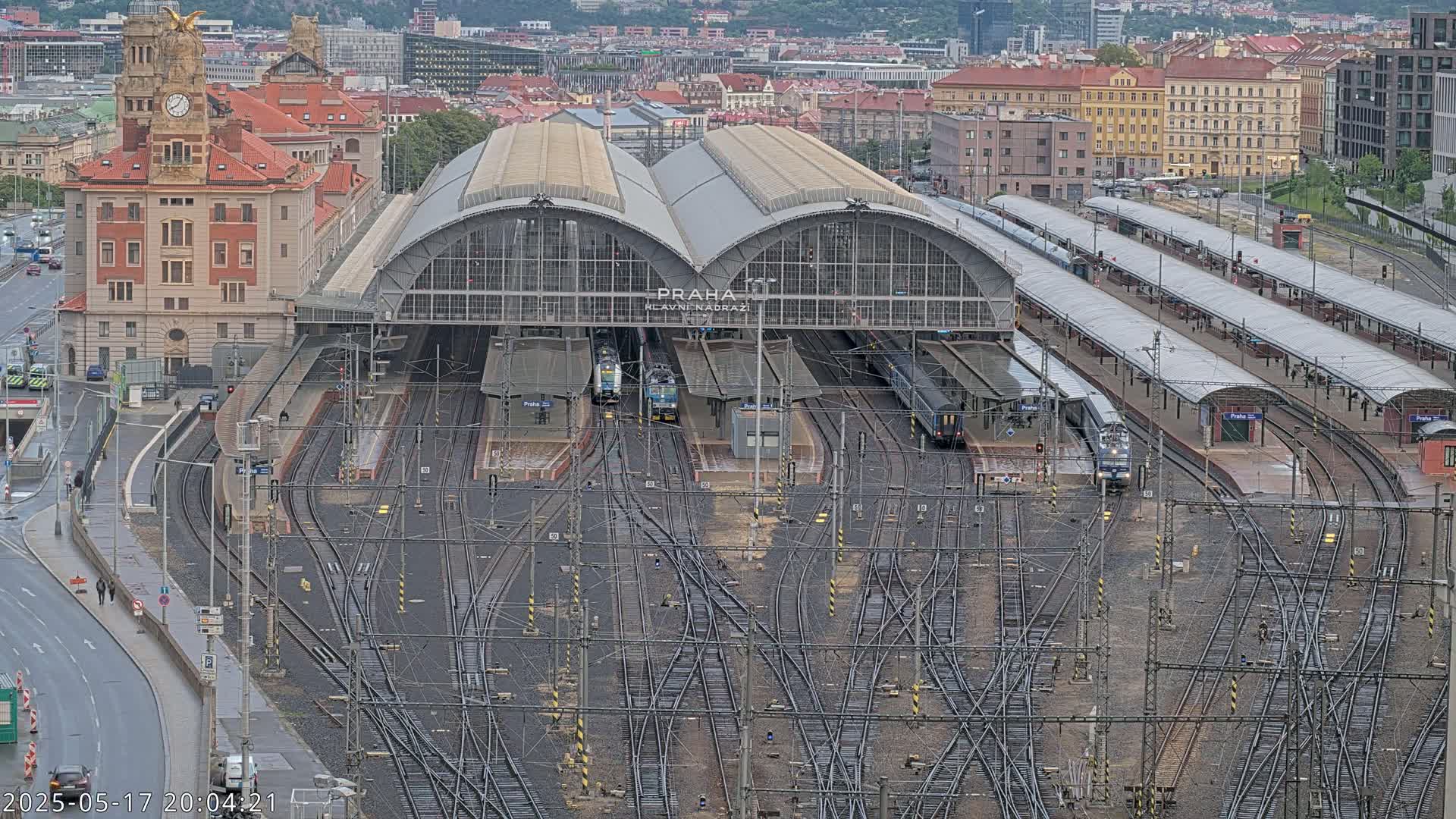 A large train station with many tracks and several trains, situated in a city under an overcast sky.