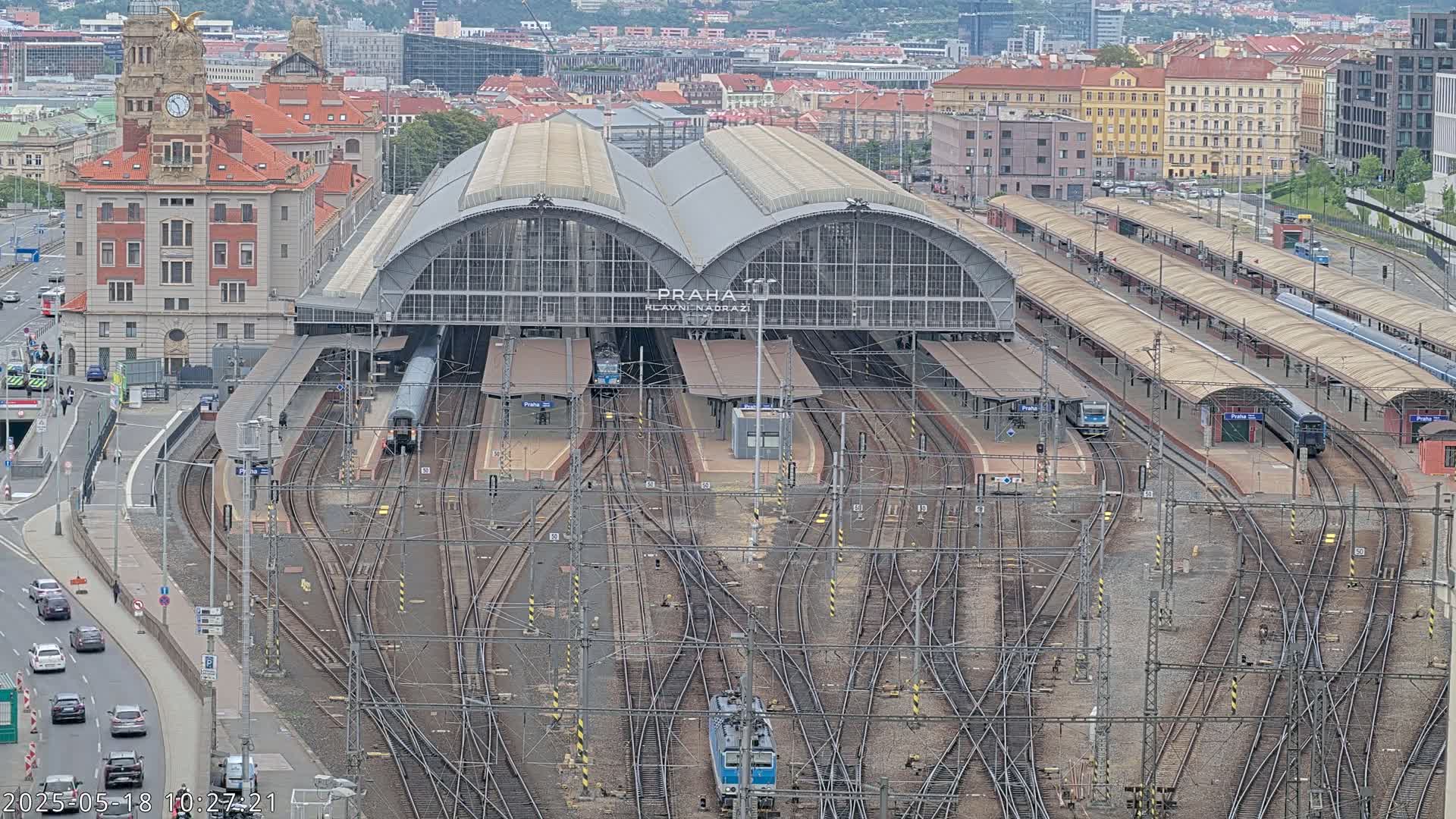 A large train station with numerous tracks and several trains, situated in a city with overcast skies.