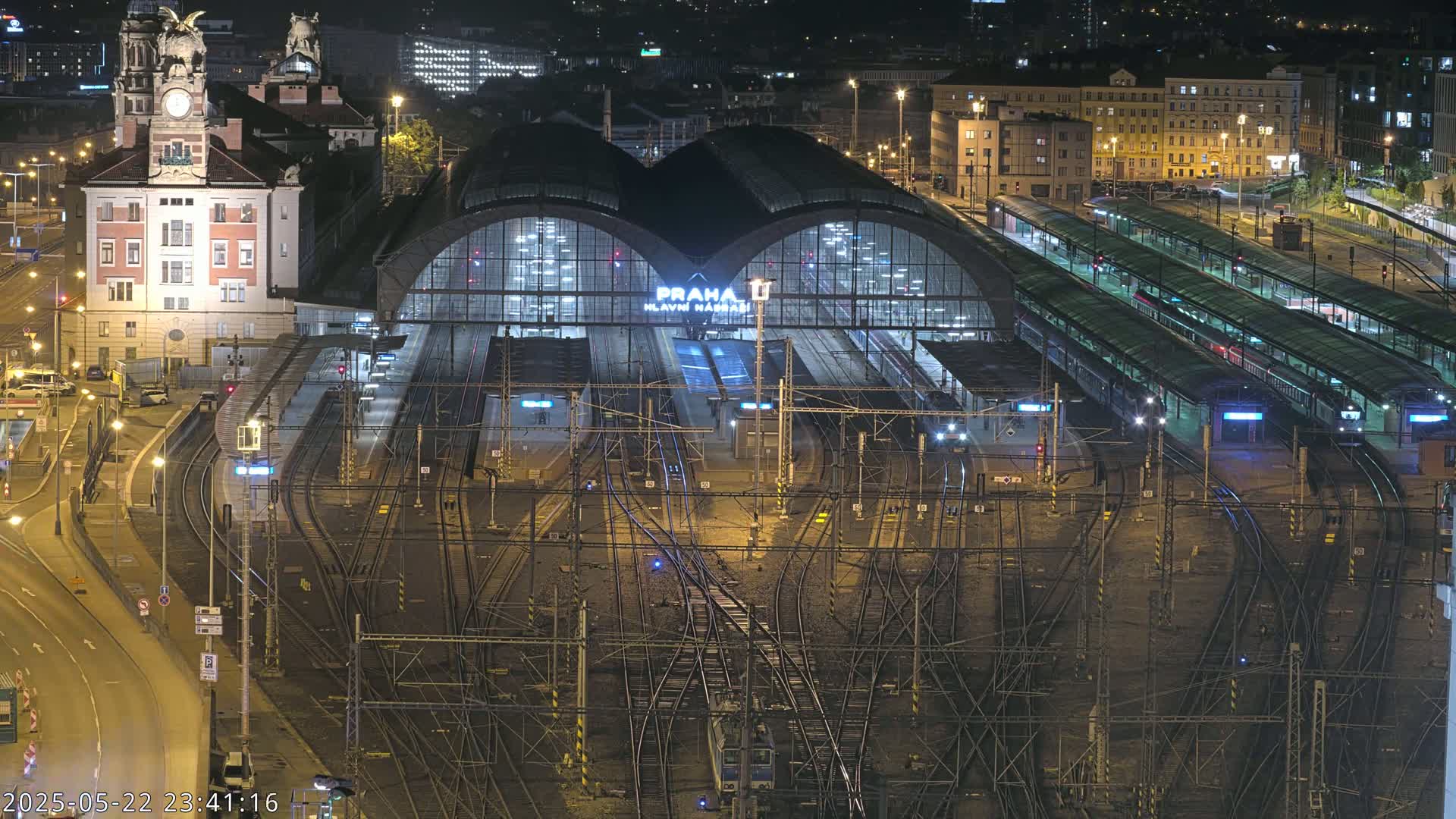 A nighttime, aerial view of a large train station with many tracks and trains, illuminated by artificial lights.