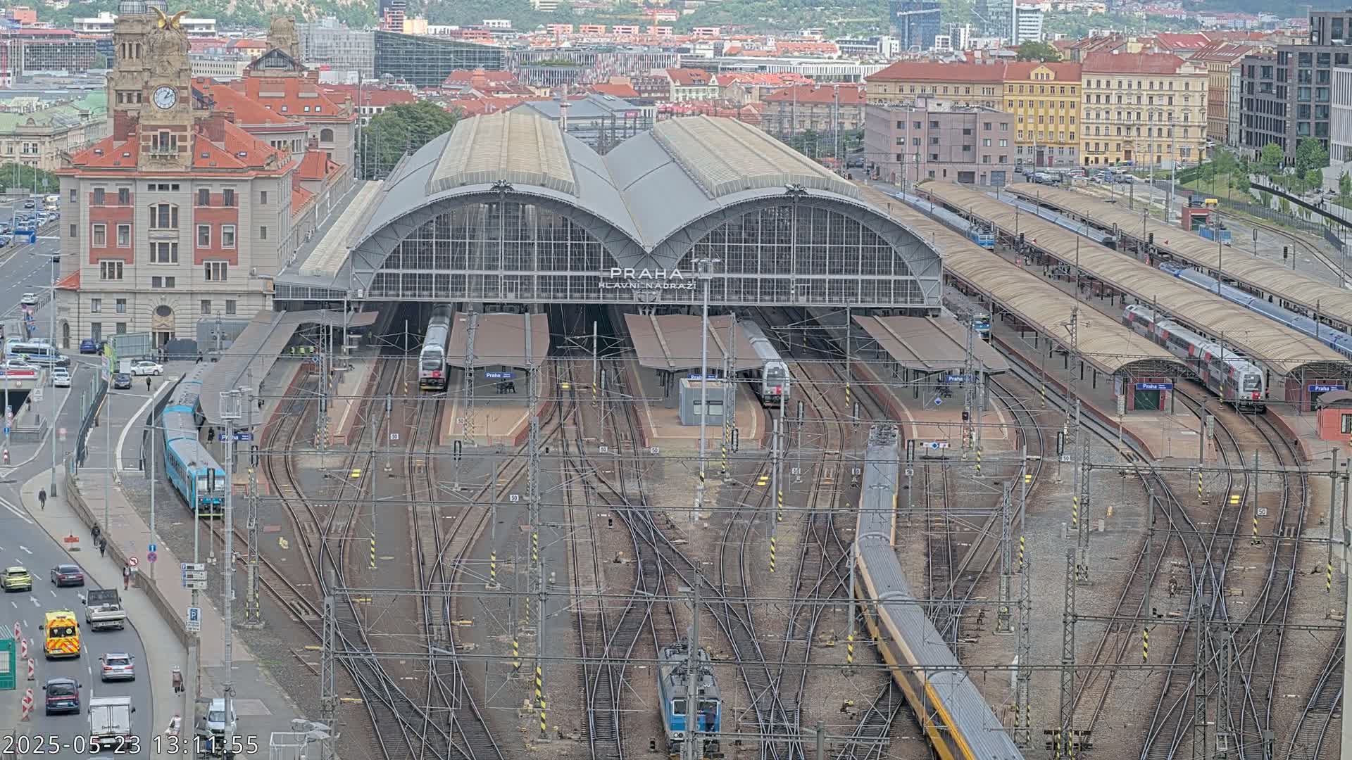 A large train station with multiple platforms and tracks, numerous trains, and a surrounding city under an overcast sky.