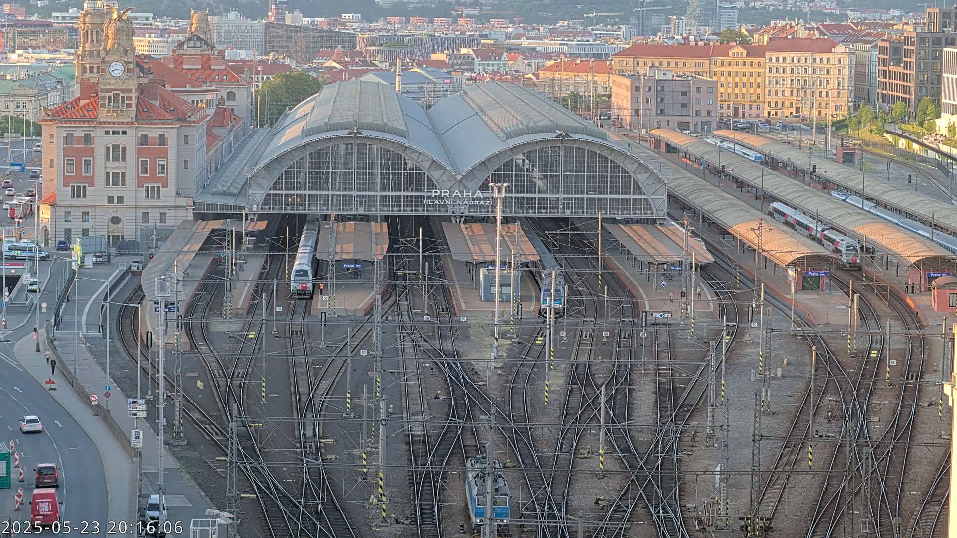 A large train station with numerous tracks and trains, surrounded by city buildings, under a mostly clear evening sky.