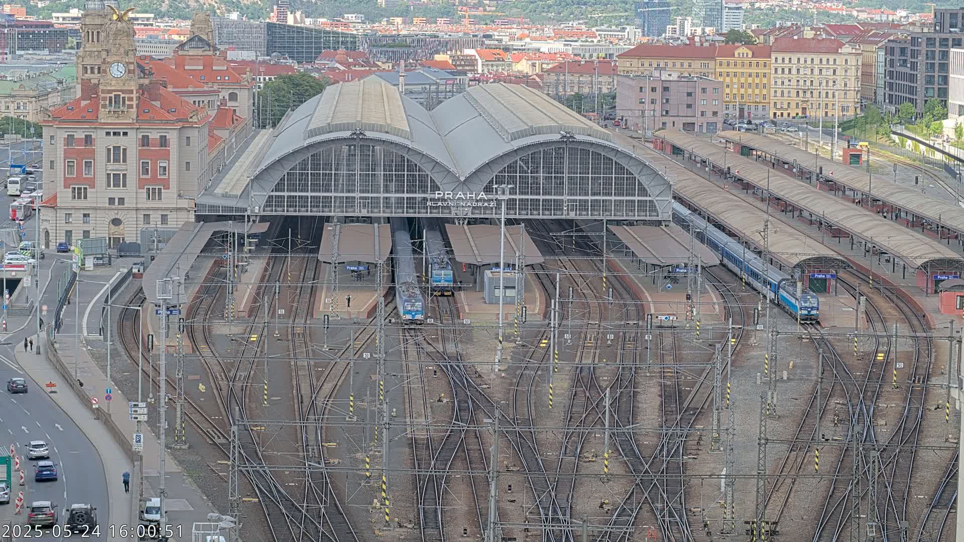 A large train station with numerous tracks and trains, surrounded by city buildings under a mostly clear sky.