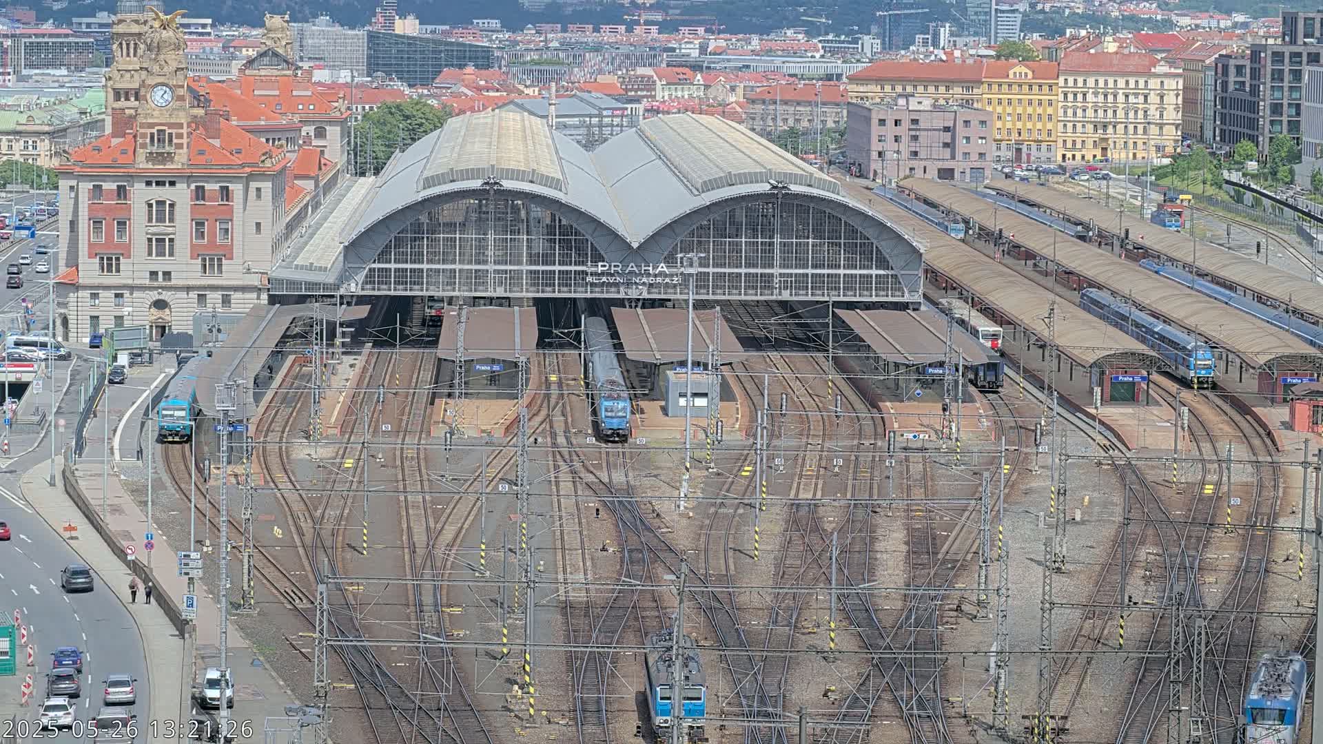 A large train station with many tracks and several trains, situated in a city on a sunny day.