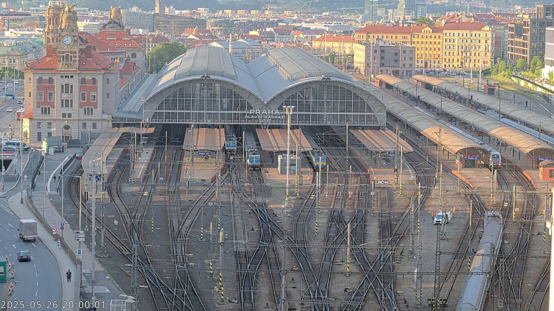 A large train station with numerous tracks and trains, under a partly sunny sky.