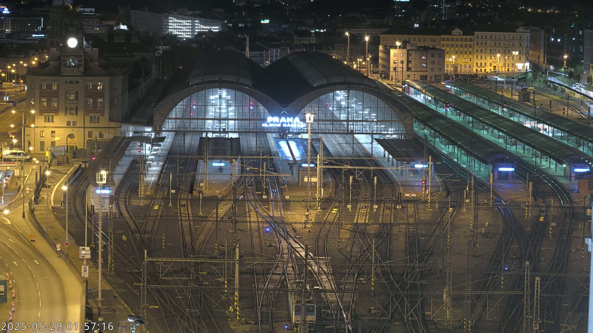 A brightly lit train station at night, with numerous tracks and platforms extending from its large, arched central building.