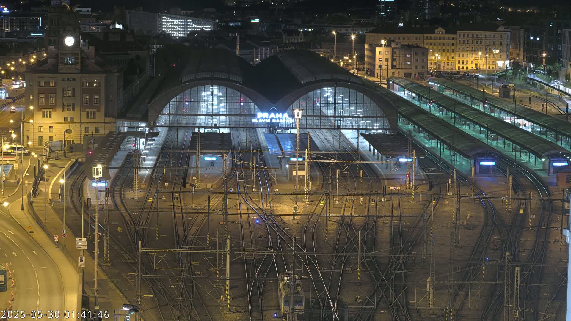 A large, illuminated train station at night, with numerous tracks and platforms extending from its central building.