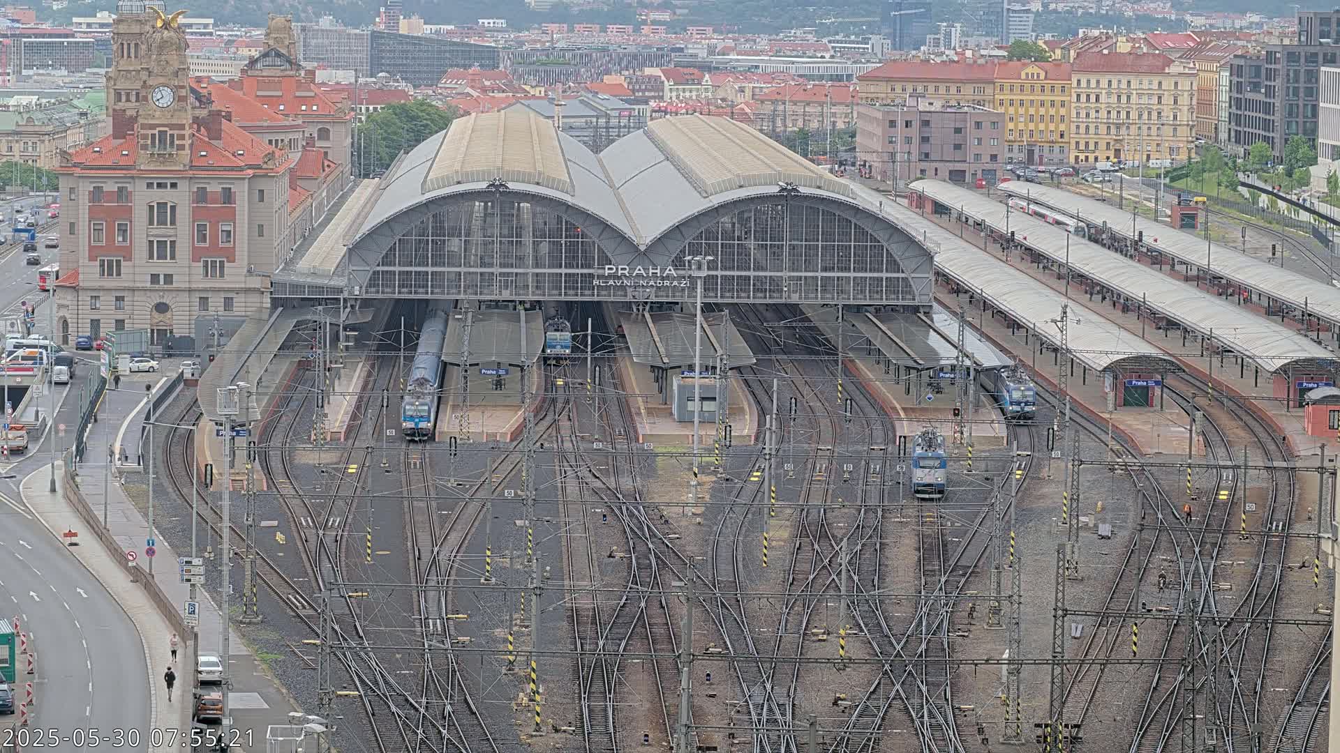 A large train station with numerous tracks and trains, situated in a city under an overcast sky.