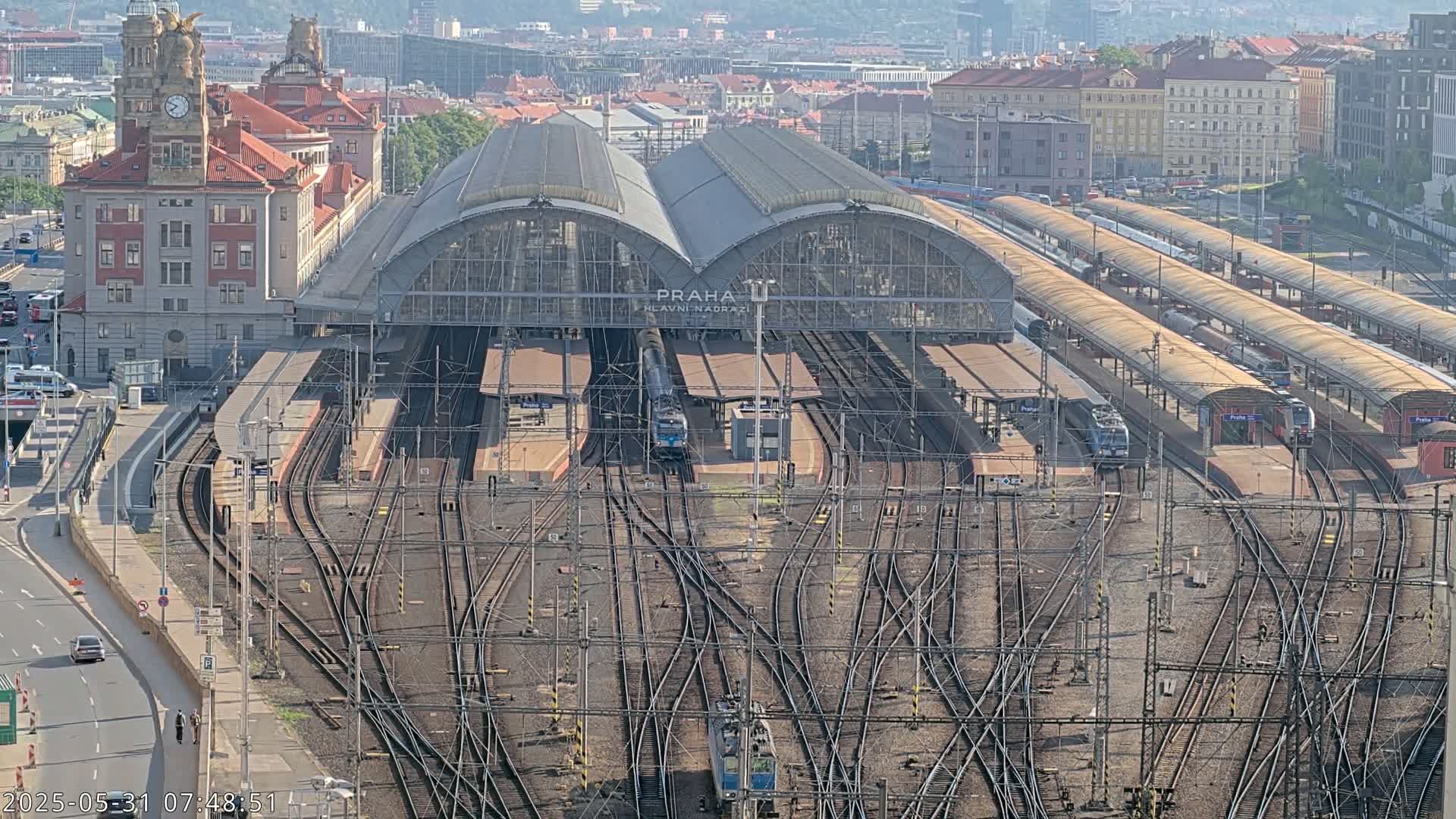 A large train station with multiple tracks and trains, viewed from above on a sunny day.