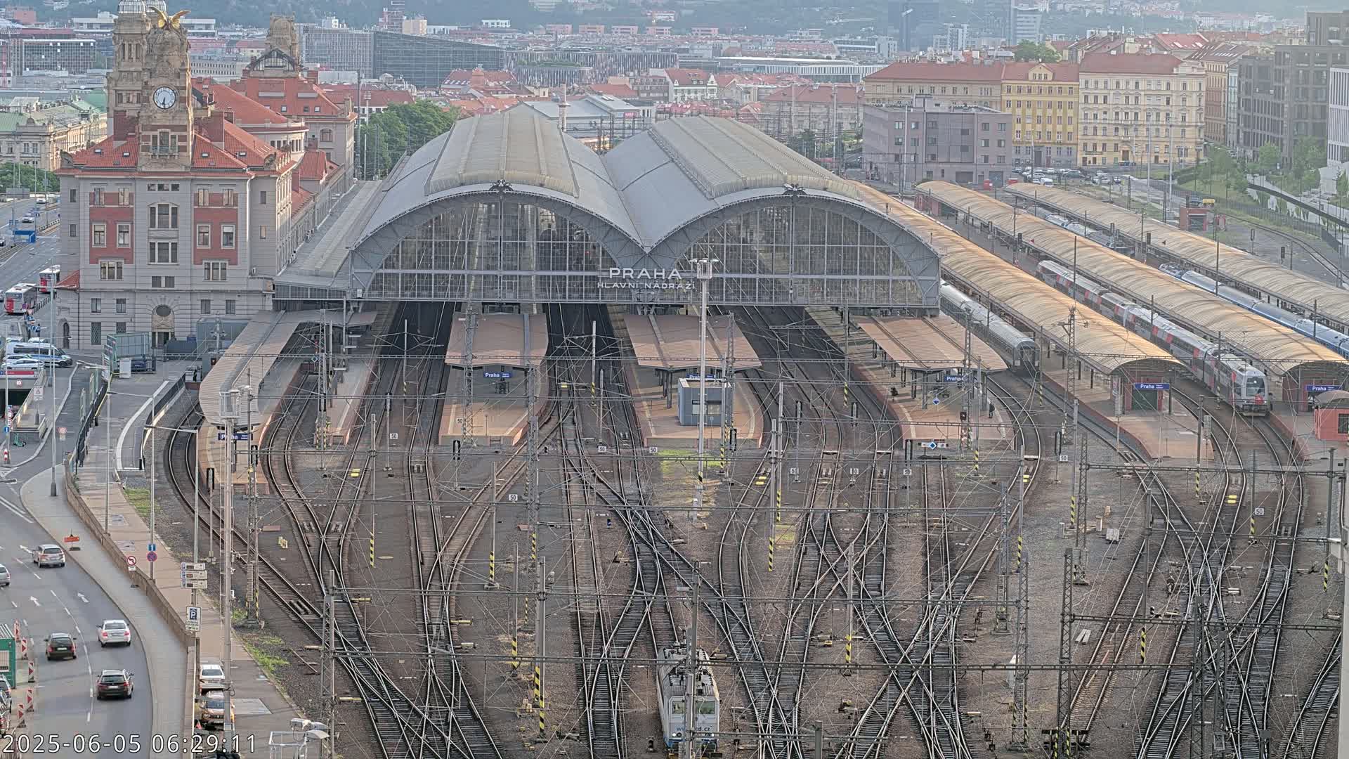 A large train station with many tracks and platforms, several trains, and a large building, under a partly cloudy sky.