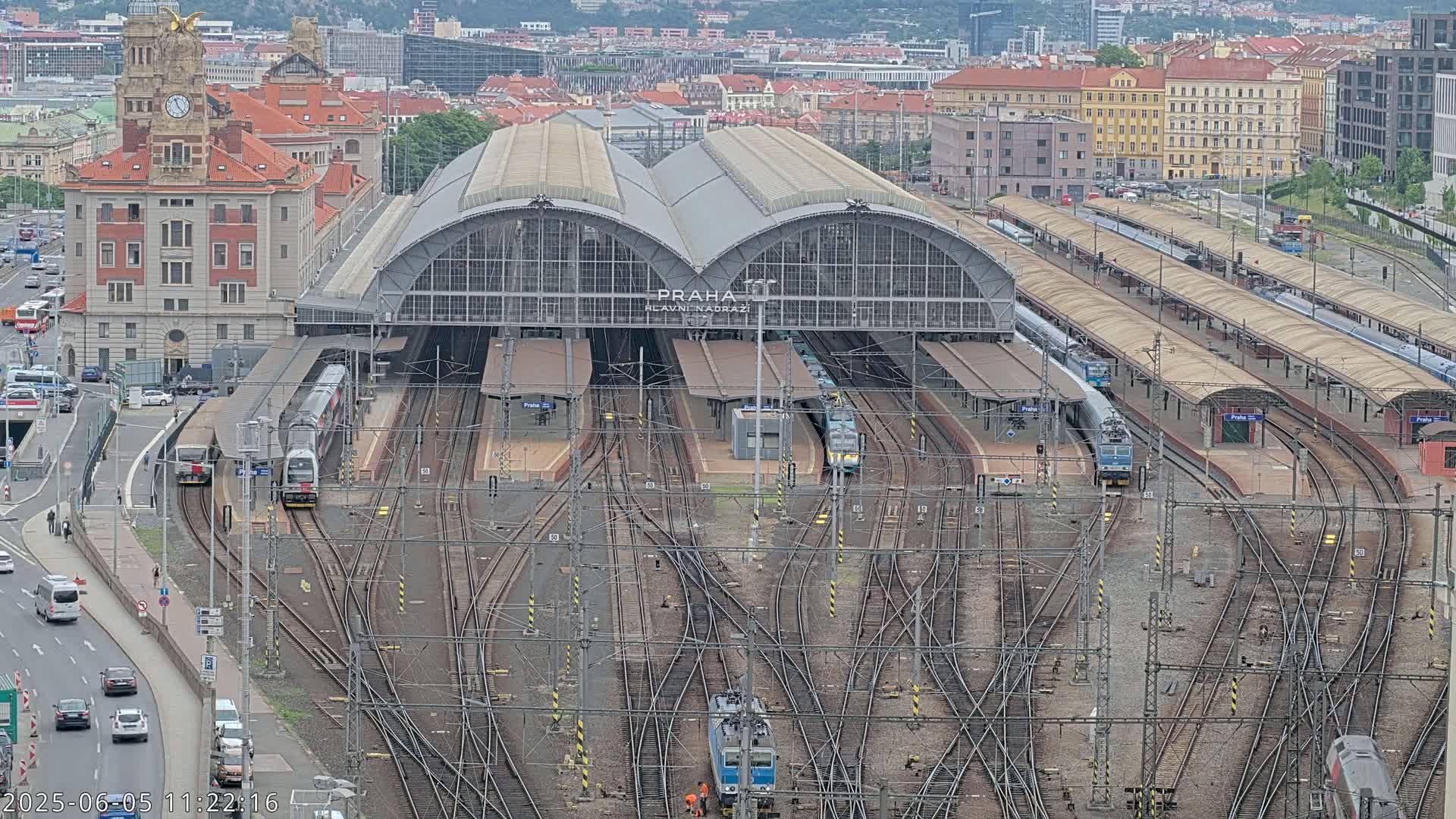 A large train station with many tracks and trains, surrounded by city buildings under an overcast sky.