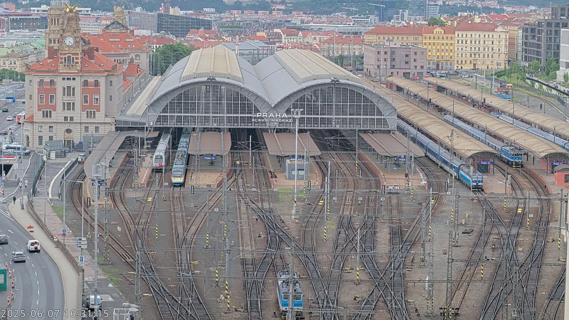 A large train station with multiple tracks and trains, situated in a city under an overcast sky.