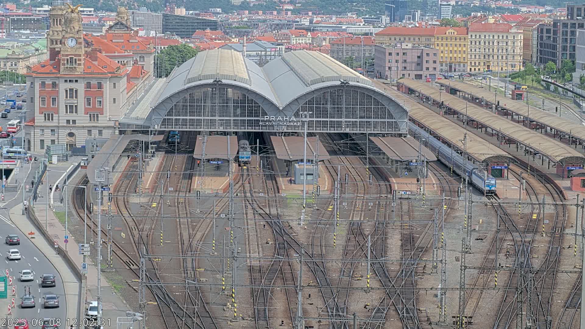 A large train station with numerous tracks and trains, situated in a city on a clear day.